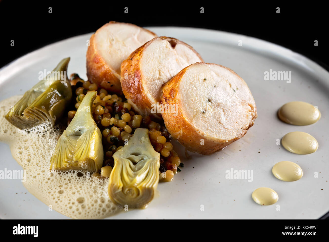 Roulade de poulet au prosciutto, l'artichaut et l'émulsion sur une assiette blanche et fond noir Banque D'Images