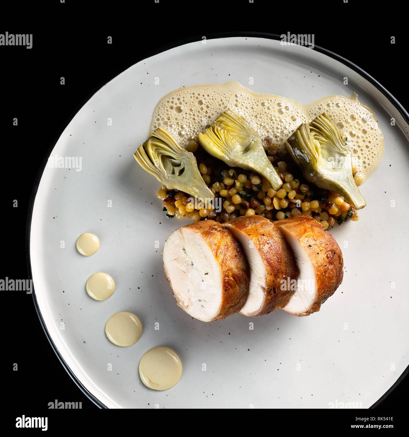 Roulade de poulet au prosciutto, l'artichaut et l'émulsion sur une assiette blanche et fond noir Banque D'Images