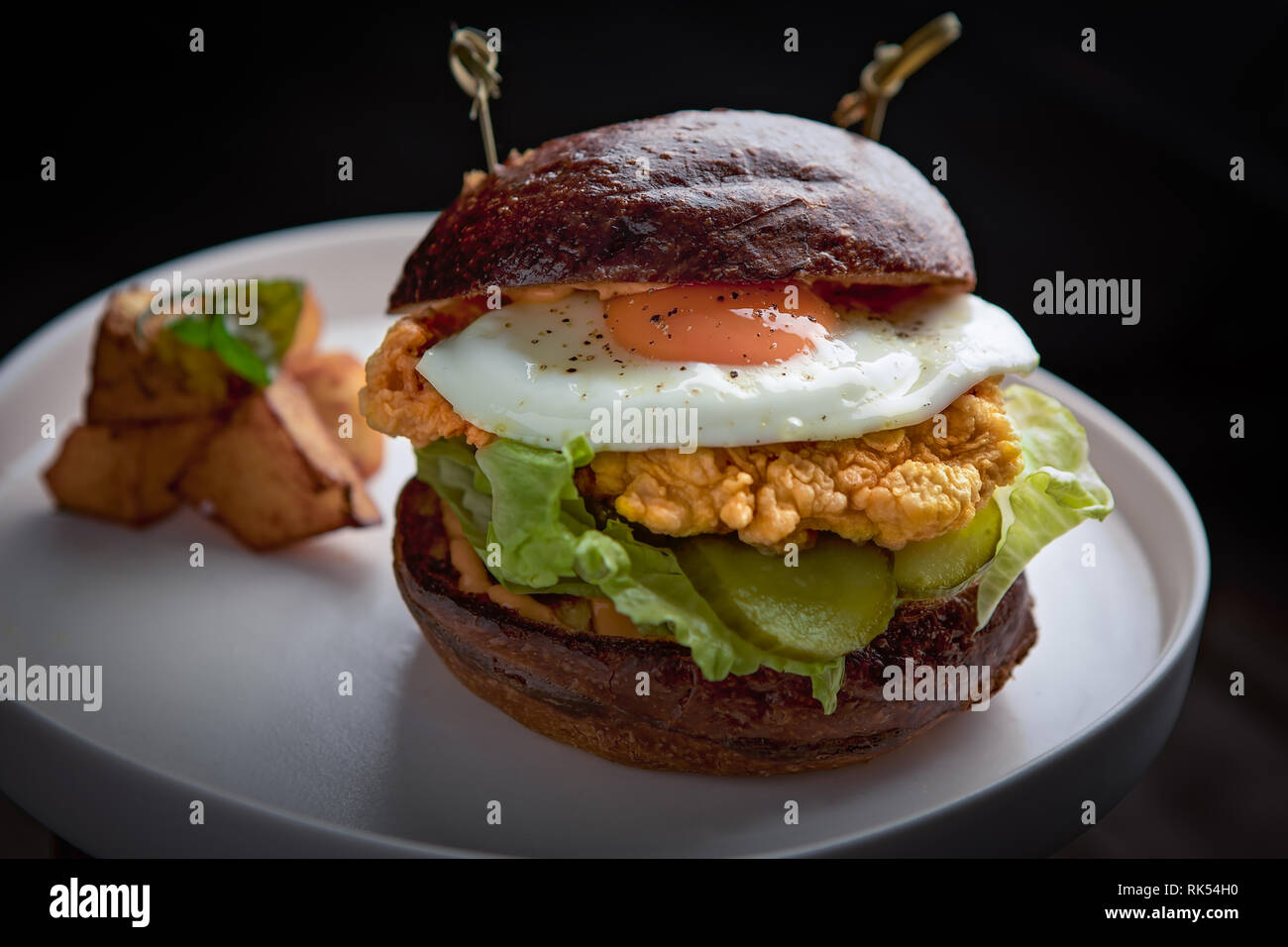 Burger de poulet avec de la laitue, cornichon, œuf et un côté de pommes de terre grillées Banque D'Images