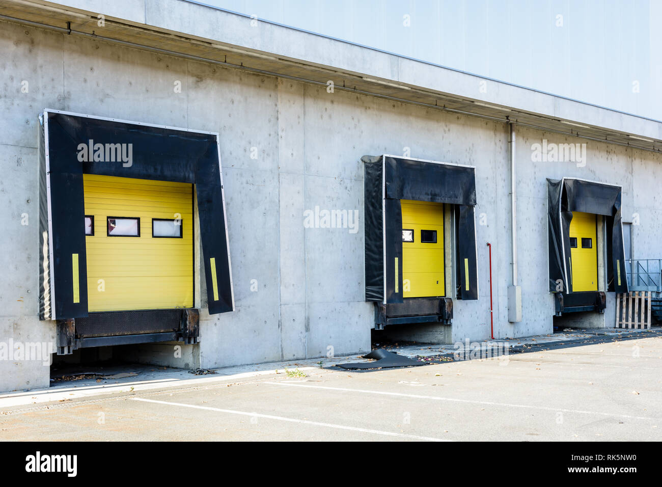 Trois quais de chargement de camions avec des joints en caoutchouc dans le mur de béton d'un entrepôt avec un volet roulant fermé la porte jaune. Banque D'Images