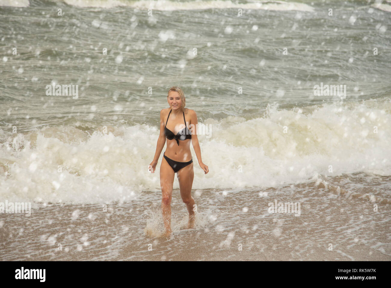 Seul jeune femme en maillot de bain marche à la mer d'hiver sous la neige qui  tombe de surf Photo Stock - Alamy