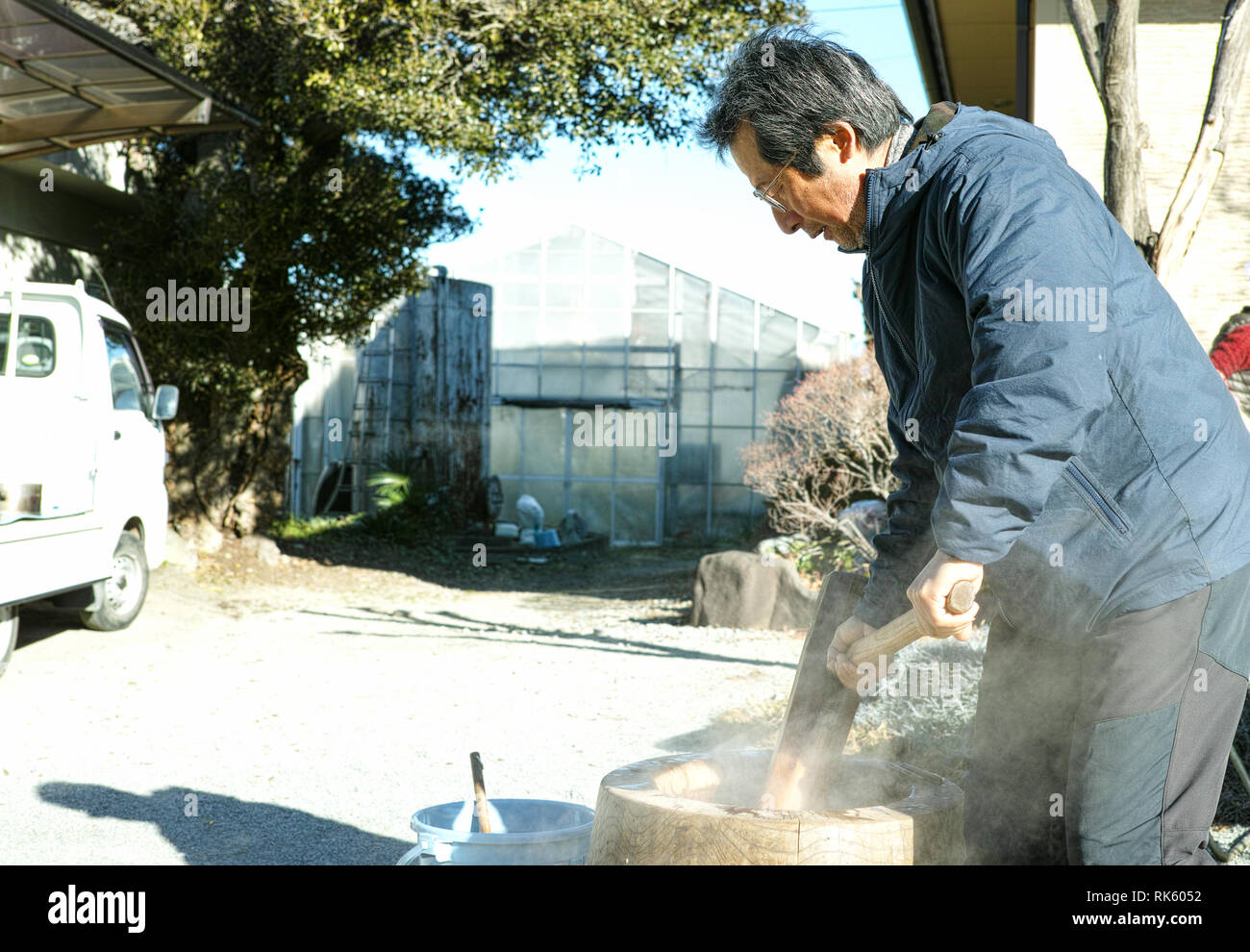 Un homme plus âgé faisant mochi dans son jardin avec le grand mortier et pilon Banque D'Images