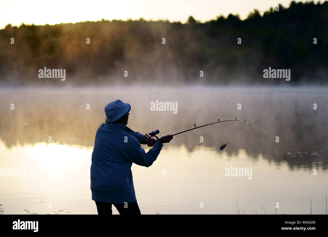 Caucasian fisherman, 50 ans, au bord du lac avec brouillard, tôt le matin juste avant le lever du soleil. Banque D'Images
