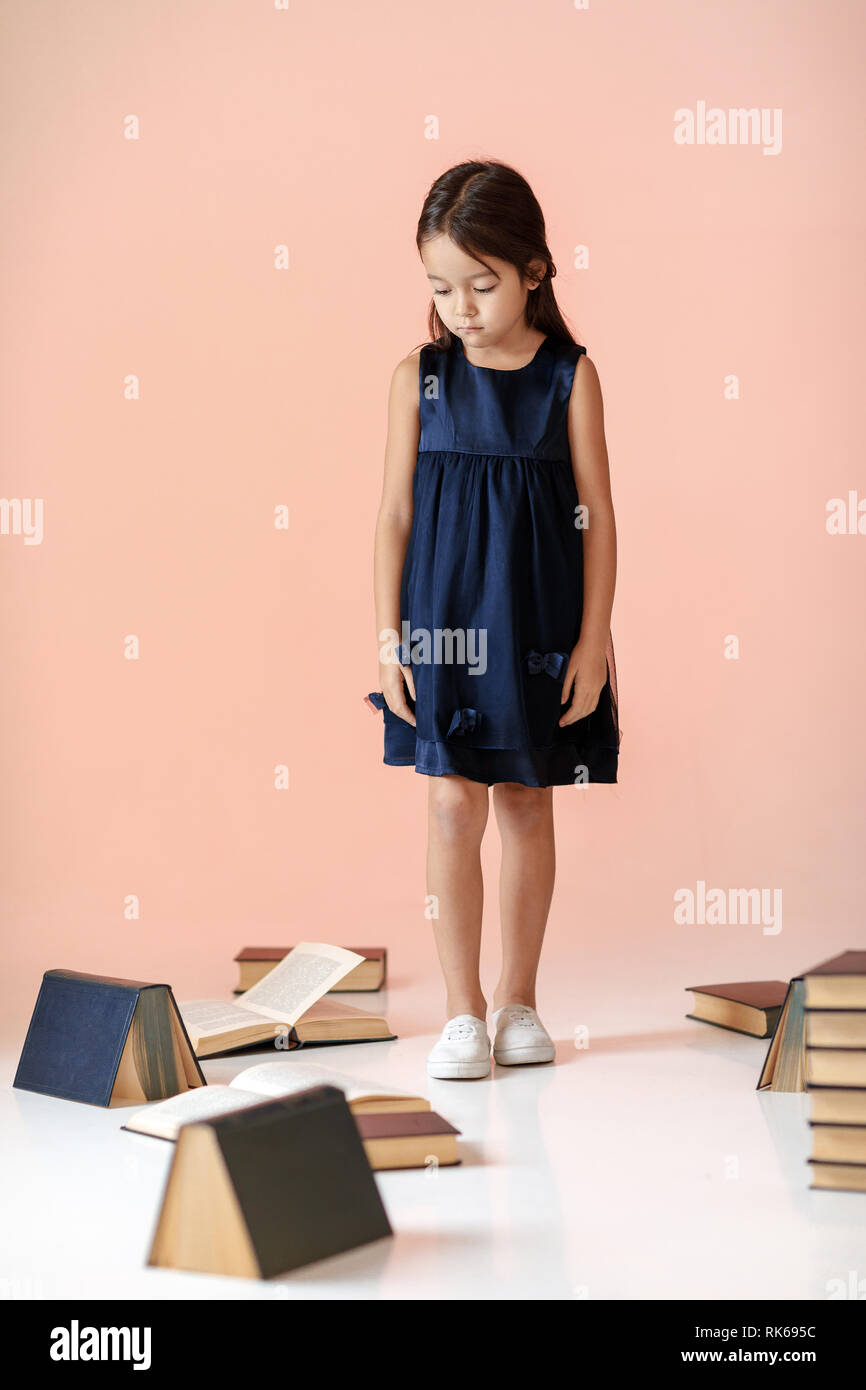 Assez triste petite fille en robe bleu foncé ne veut pas lire des livres. enfant et beaucoup de livres. Les enfants et l'éducation. Banque D'Images