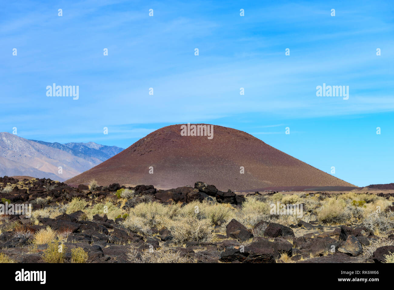 Volcan éteint qui s'élève sur le paysage rocheux sous ciel bleu avec des montagnes au-delà. Banque D'Images