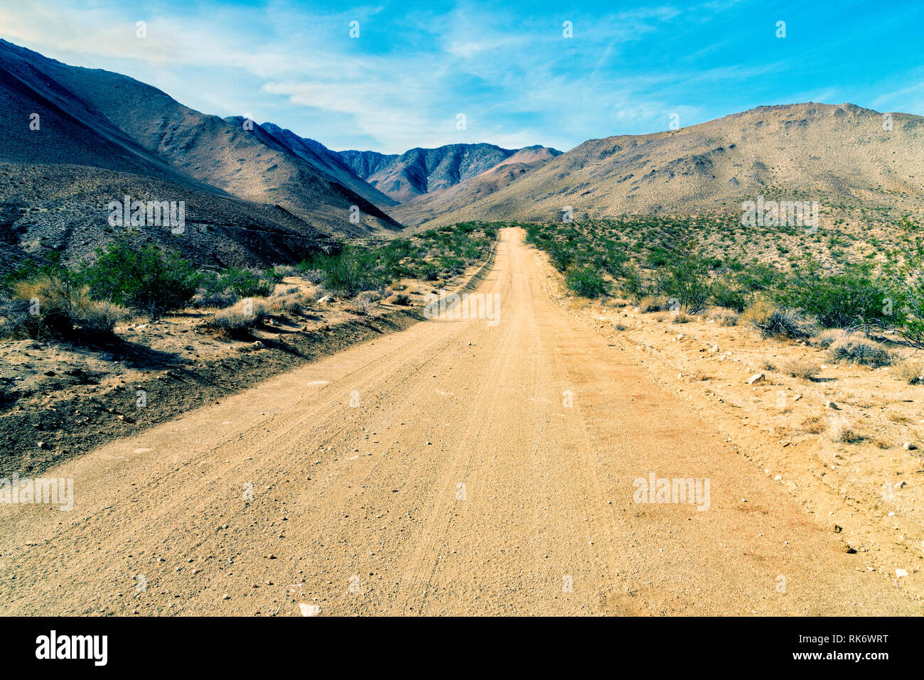 Le désert aride à la route de terre qui mène dans des montagnes du désert au-delà sous ciel bleu. Banque D'Images