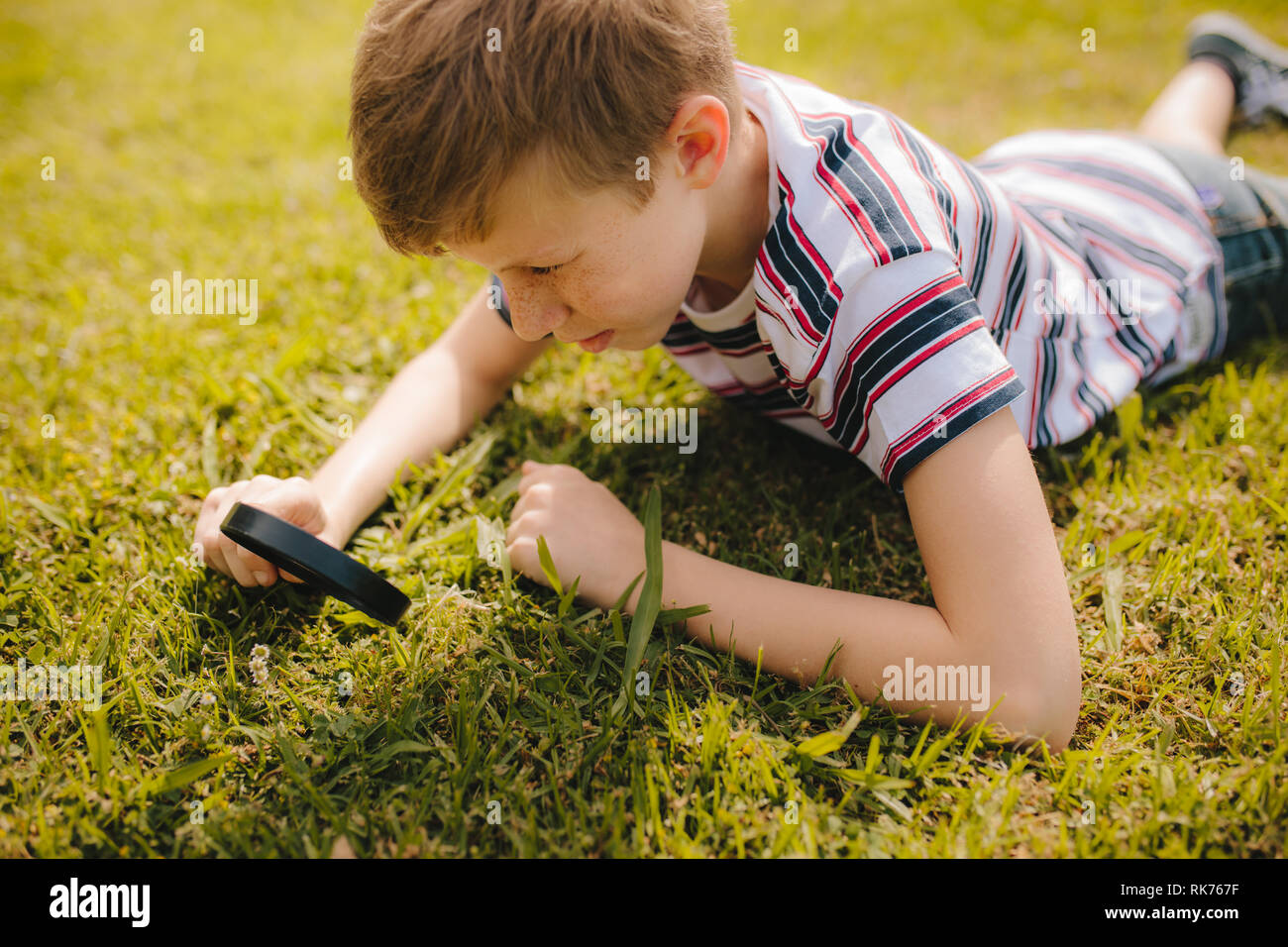 Young boy explorer jardin herbe avec sa loupe. Jeune garçon à la loupe à travers à l'herbe. Banque D'Images