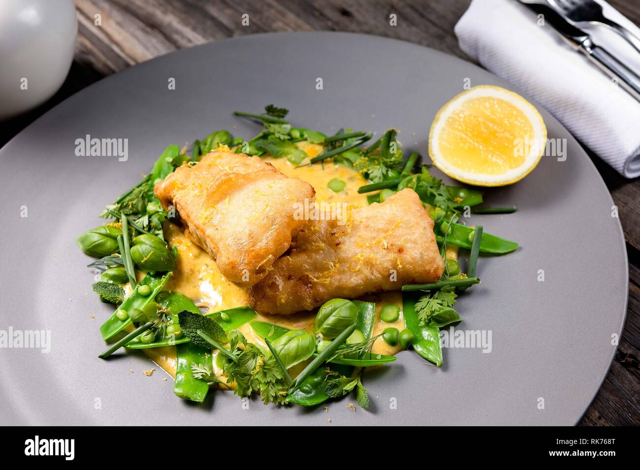 En-cas de poisson blanc frit tendre servi dans une sauce crémeuse sur un lit ou des greens Banque D'Images