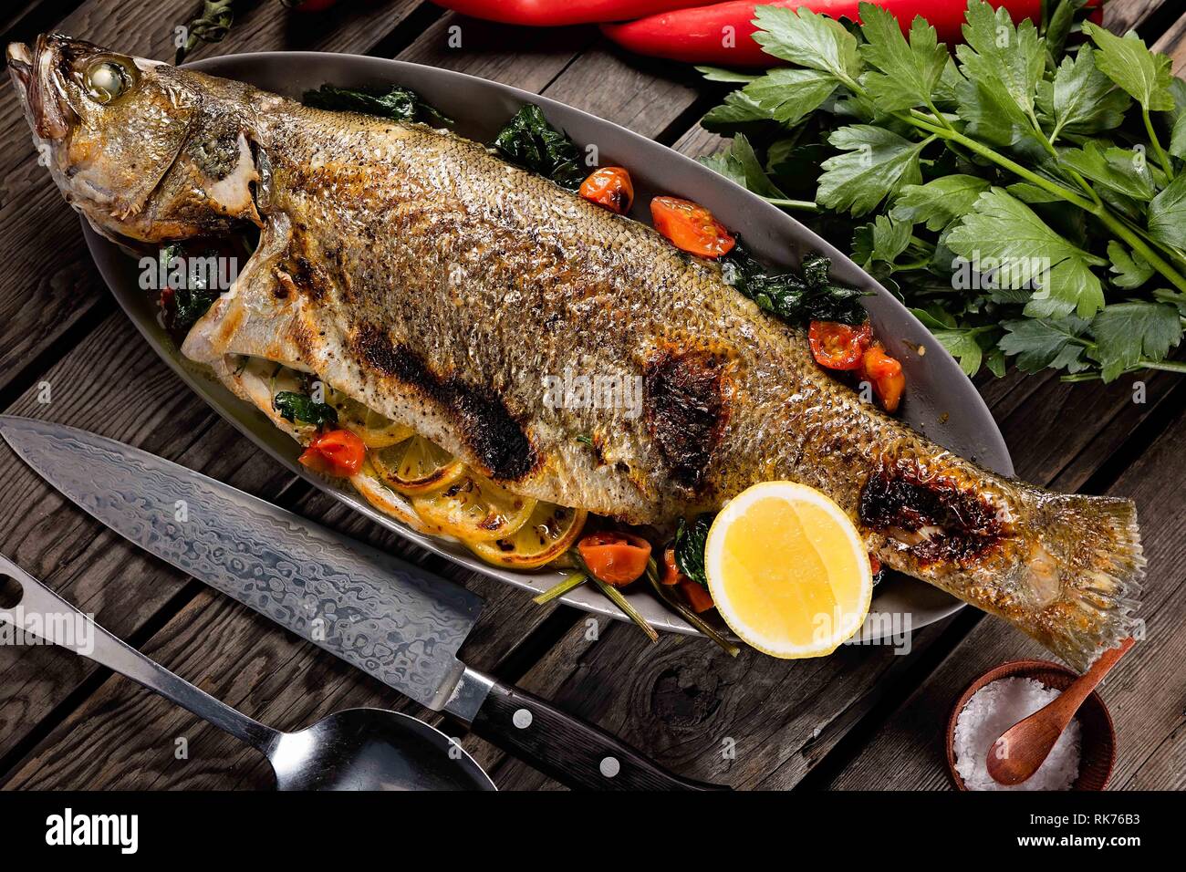 Beau poisson entier grillé et servi sur une poêle en métal avec des tomates, du citron et des herbes Banque D'Images