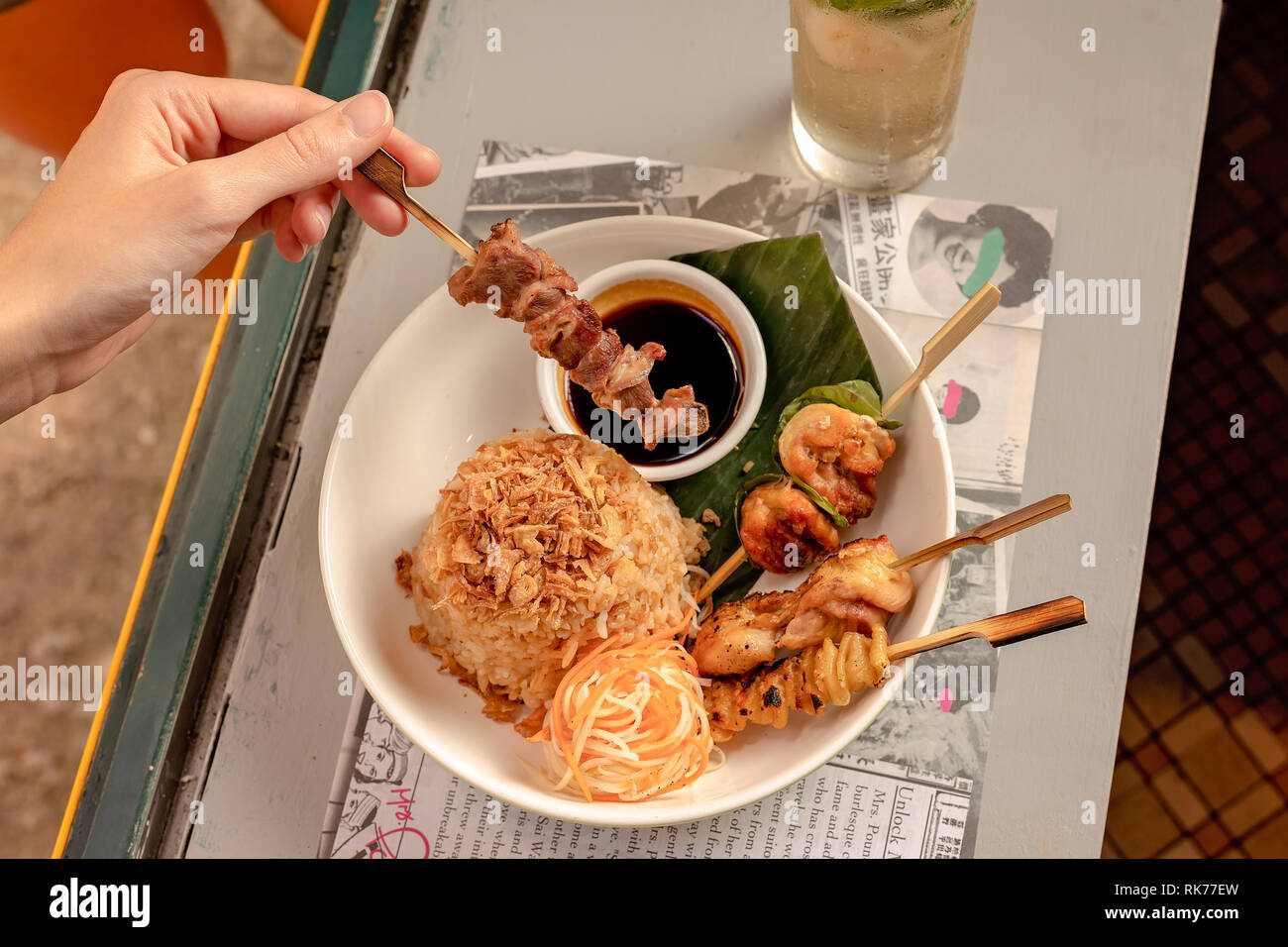 Main tenant une brochette d'un ensemble de viande servi avec du riz frit, des légumes et de la sauce soja Banque D'Images
