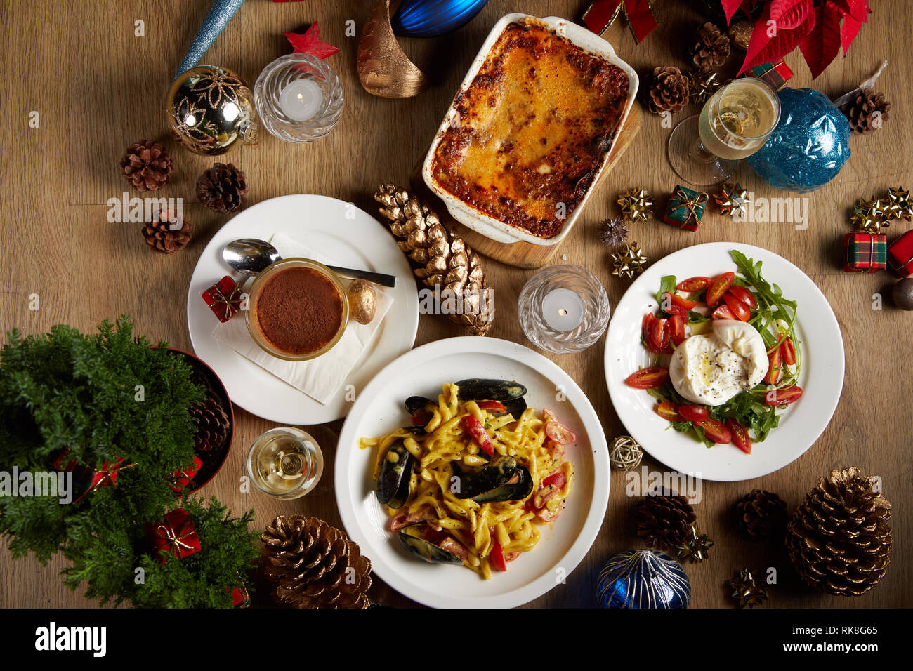 Photo à plat d'une table de Noël avec lasagnes, pâtes aux moules, salade burrata et tiramisu servi avec un peu de vin mousseux Banque D'Images