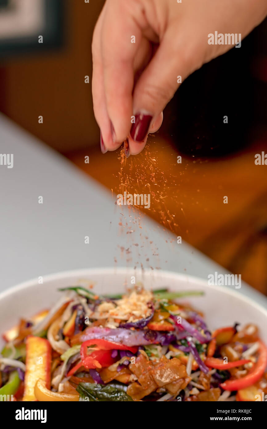 Saupoudrer à la main de délicieuses épices sur un plat thaïlandais Banque D'Images