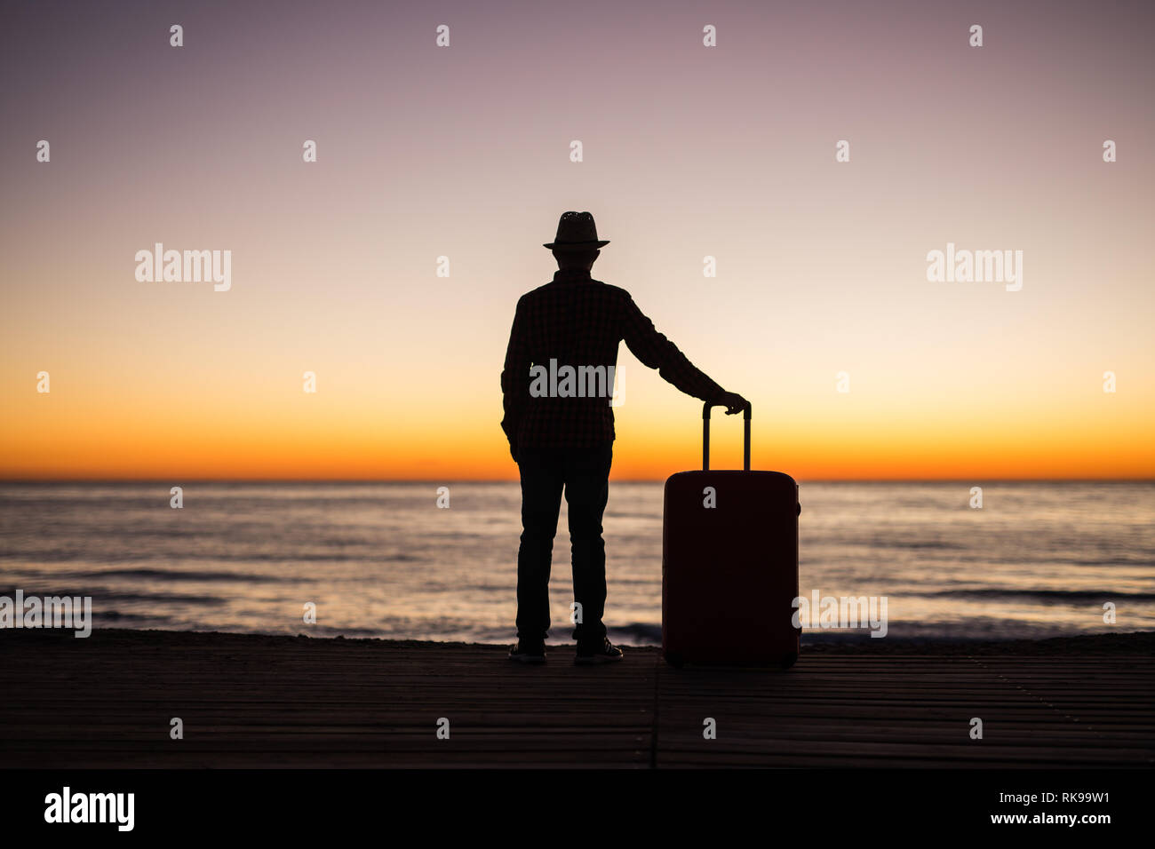 Vacances, l'été et travel concept - jeune homme d'ossature avec valise au coucher du soleil près de la mer Banque D'Images