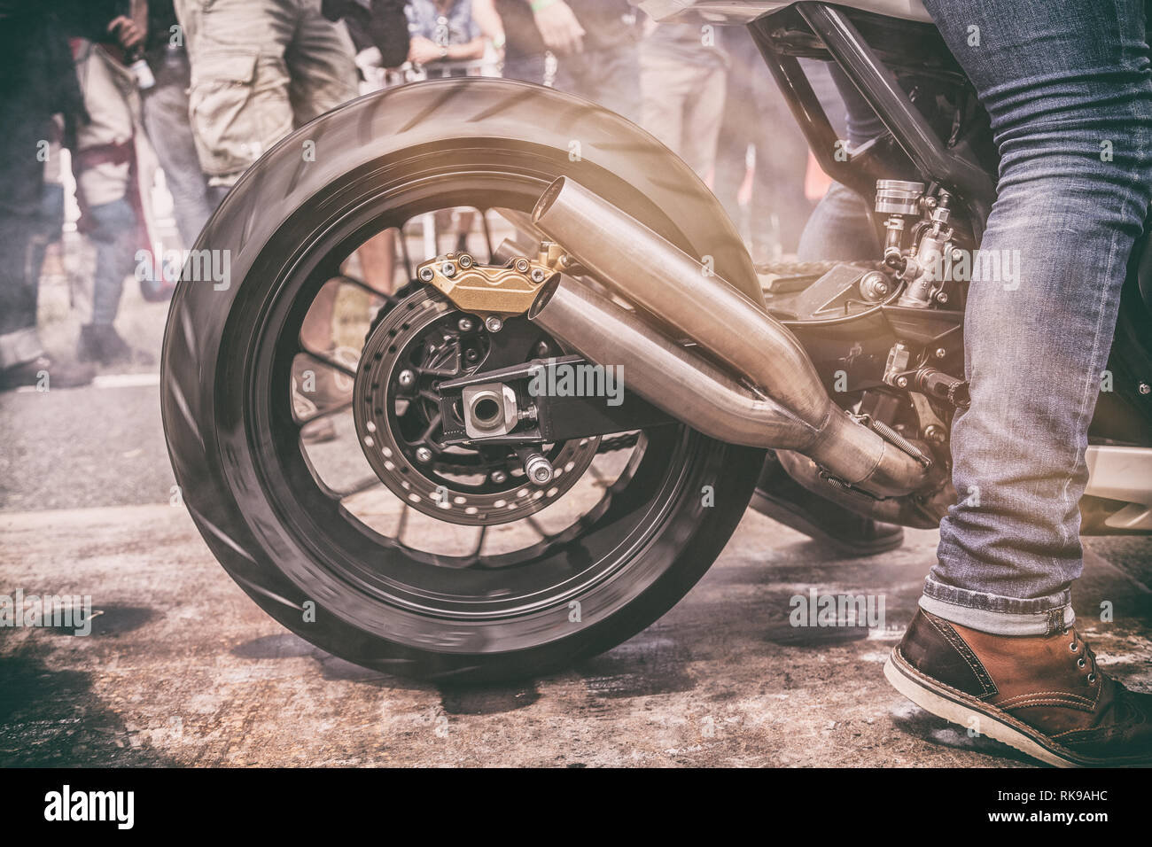 Burnout moto et glissement des roues arrière au début d'une course de glisser entouré par des tiers Banque D'Images