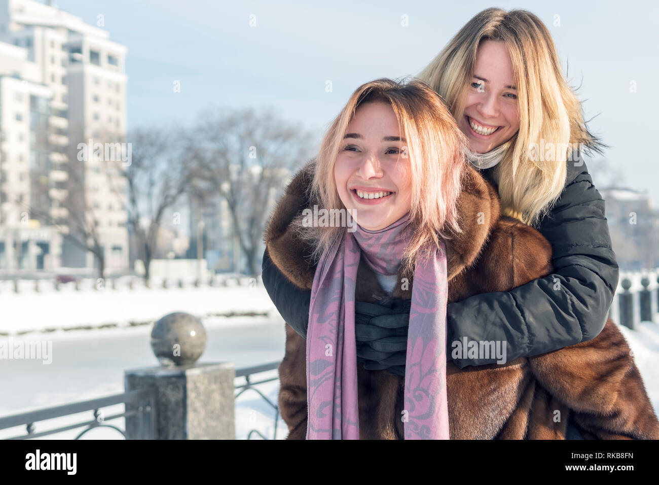 Les amies se racontent autour, de sauter sur le dos de l'autre tout en marchant à travers un parc d'hiver à proximité d'une rivière gelée Banque D'Images