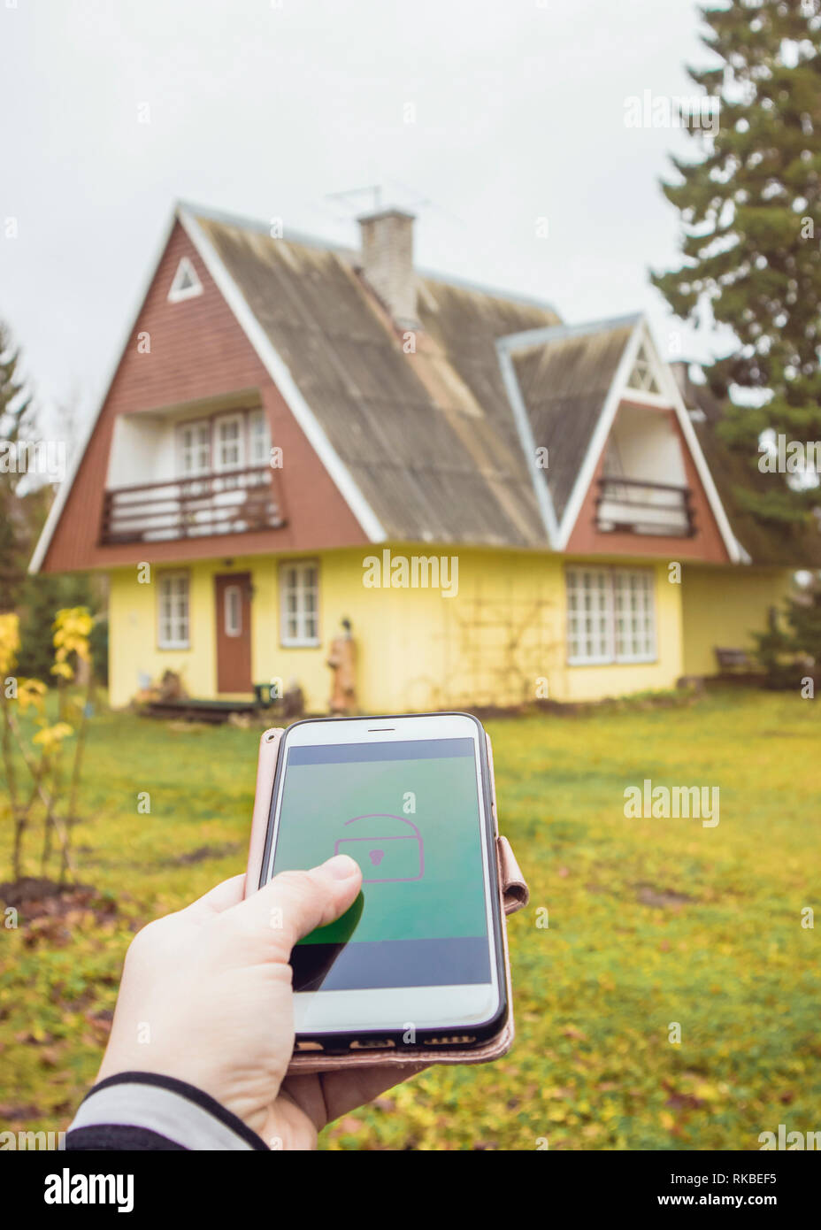 Personne part appuyer sur le bouton de verrouillage/déverrouillage à distance sur smartphone app pour ouvrir/fermer la porte de la chambre d'accueil en milieu rural. Technologie concept de vie moderne. Banque D'Images