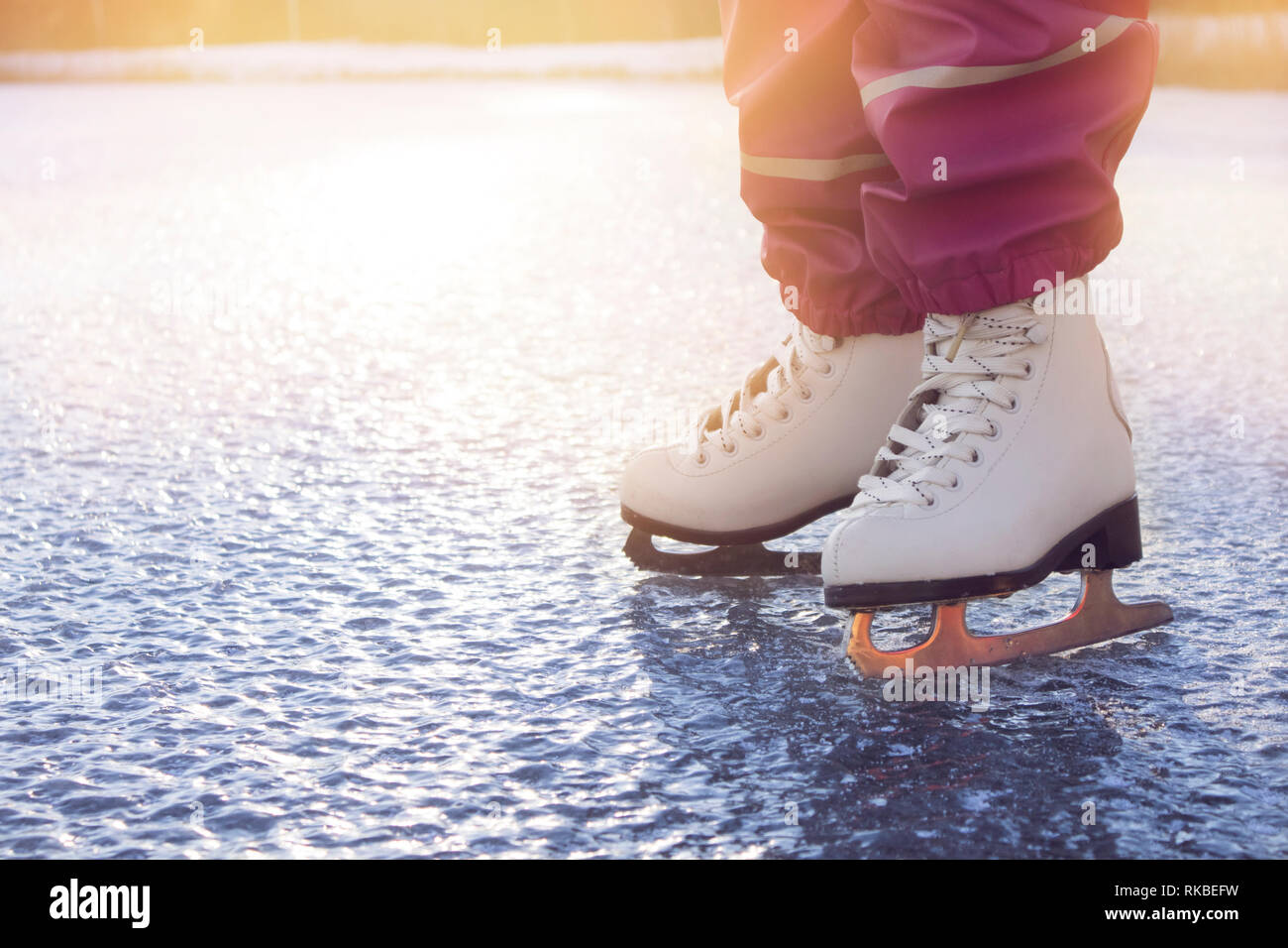 Vue rapprochée des jeunes 4 ans, fille, vêtu de blanc des patins, patinage sur le lac gelé dans la nature à l'extérieur par temps froid d'hiver ensoleillée journée. Hobby concept. Banque D'Images