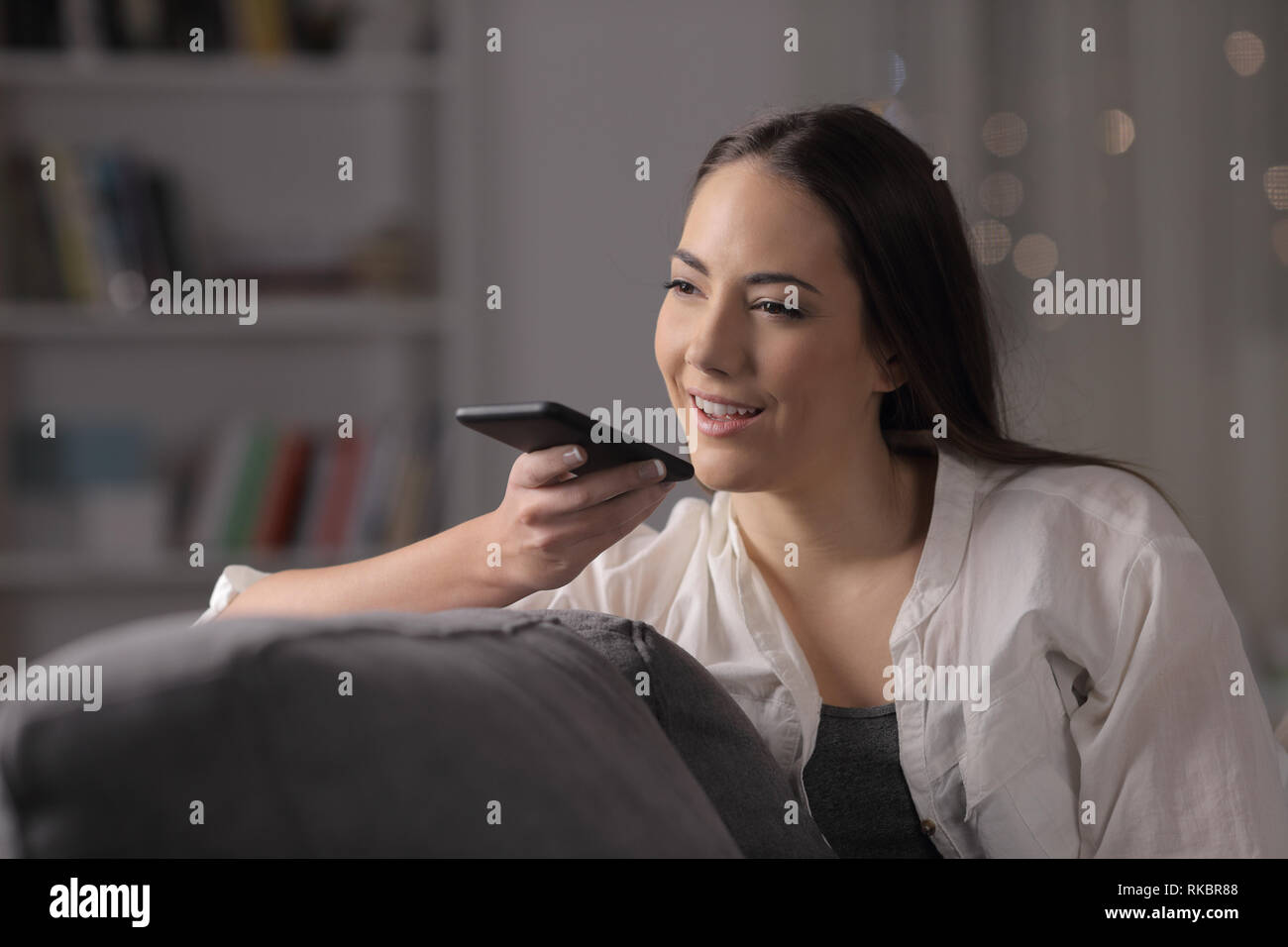 La femme de la nuit en utilisant la reconnaissance vocale téléphone assis sur un canapé dans la nuit à la maison Banque D'Images