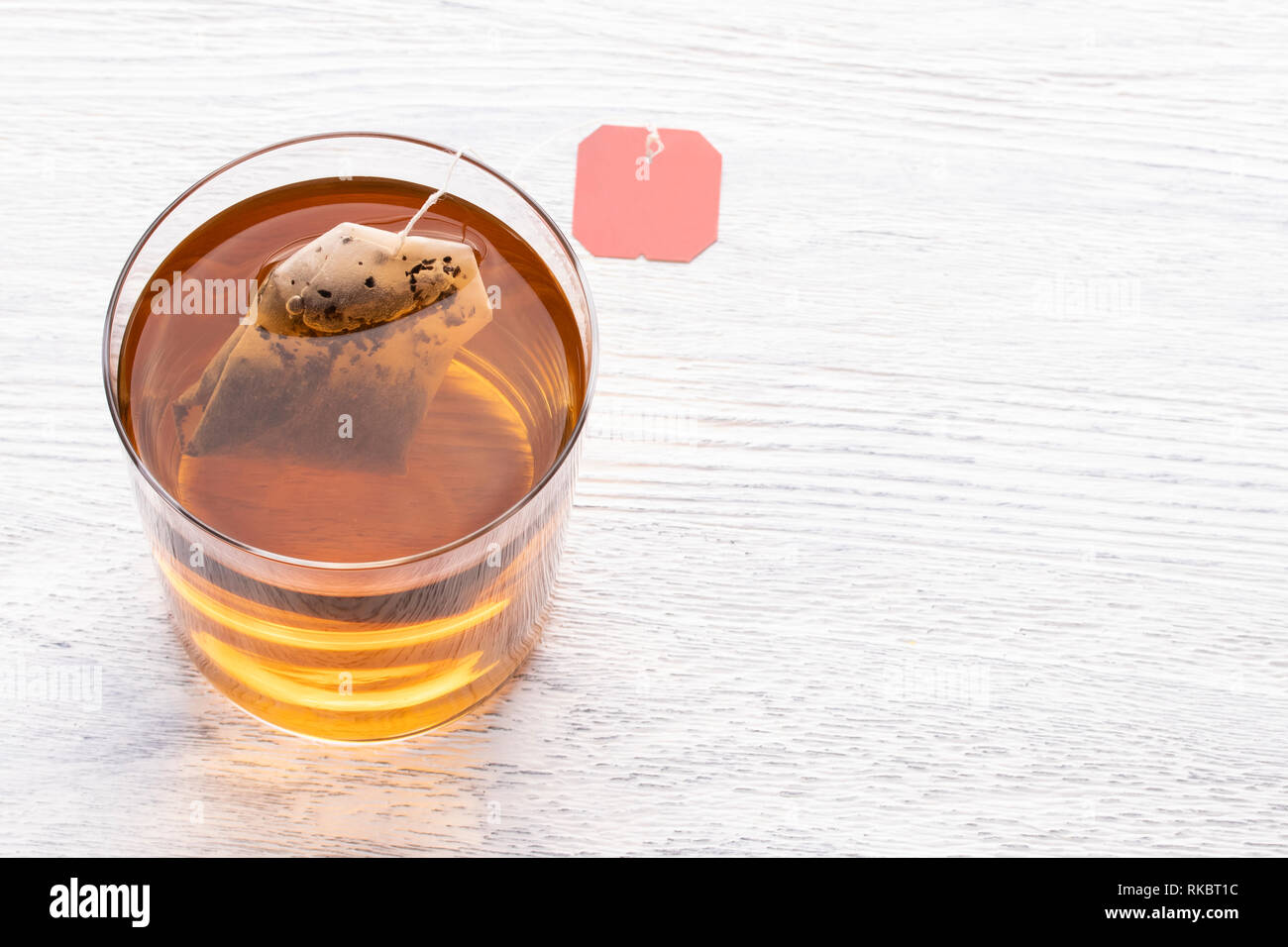 Sachet de thé dans une tasse en verre transparent avec de l'eau chaude sur une table en bois blanc Banque D'Images