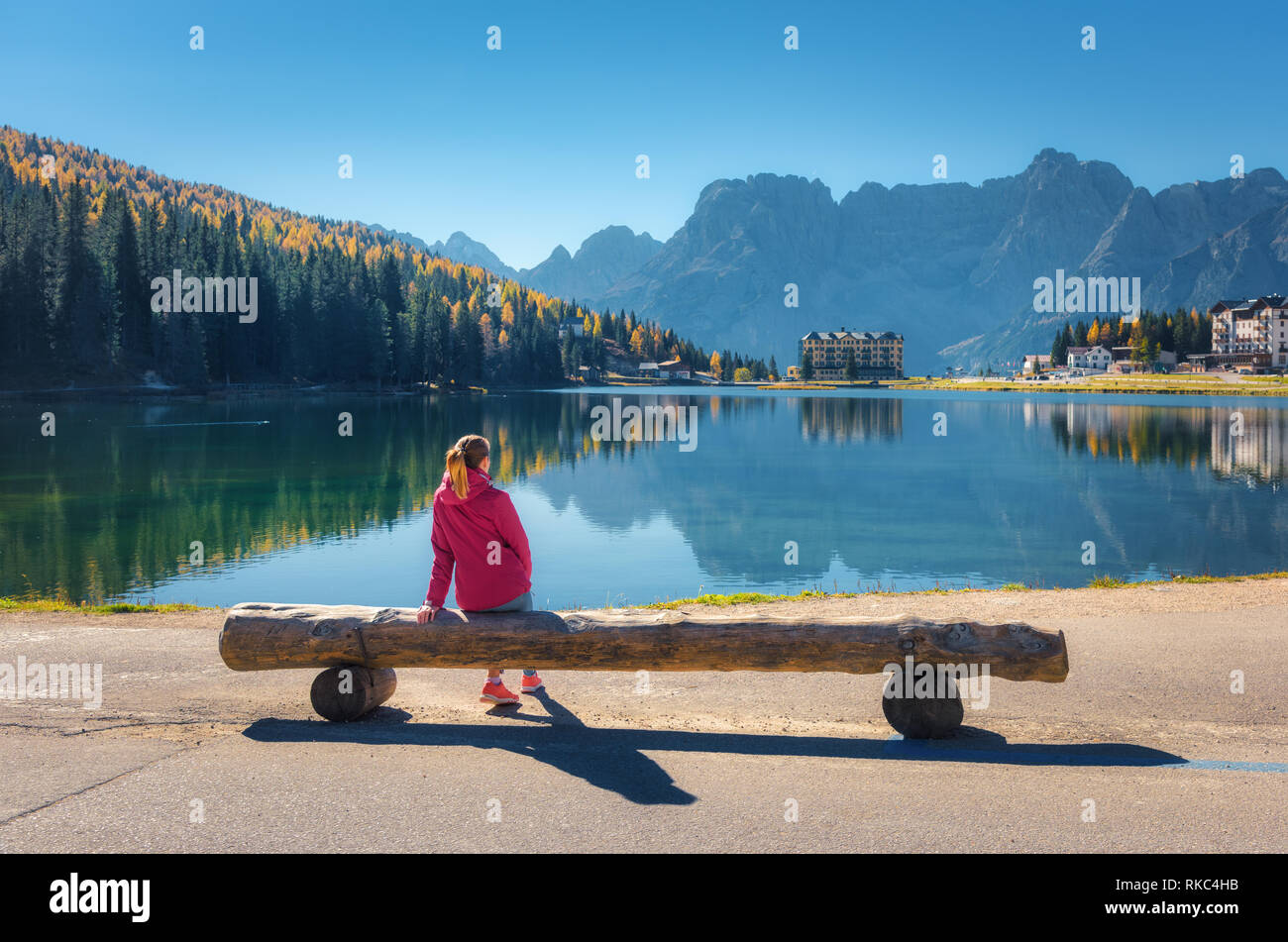 Jeune femme assise sur le banc en bois sur la côte du lac de Misurina au coucher du soleil en automne. Dolomites, Italie. Paysage avec Girl in red jacket, reflec Banque D'Images