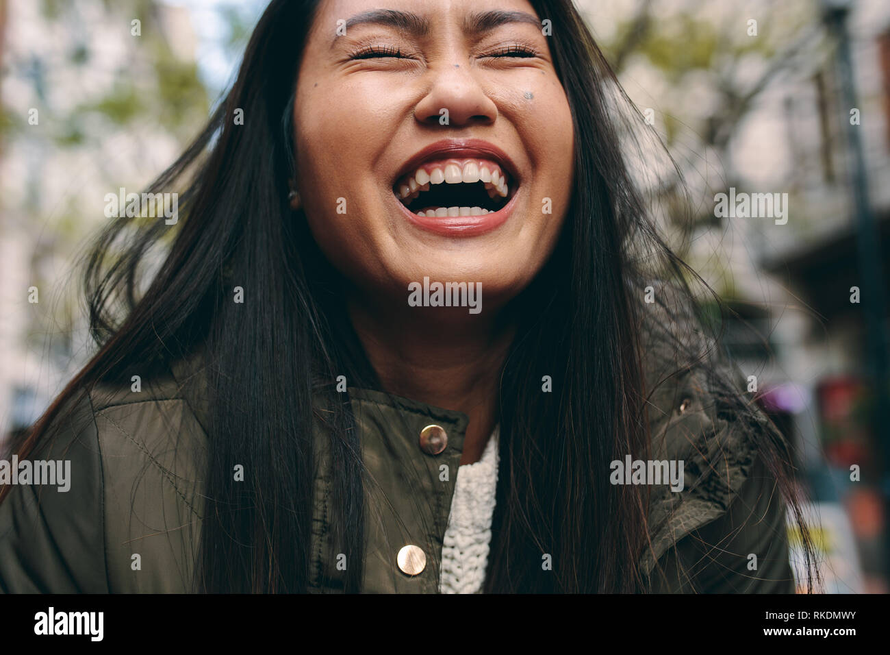 Portrait d'une femme en riant avec les yeux fermés. Cropped shot d'une femme asiatique rire standing outdoors. Banque D'Images
