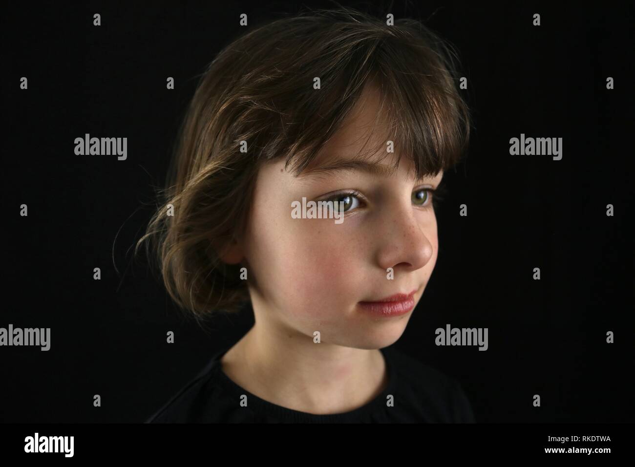 Portrait d'une fille brune aux yeux verts vu de côté sur un fond noir Banque D'Images