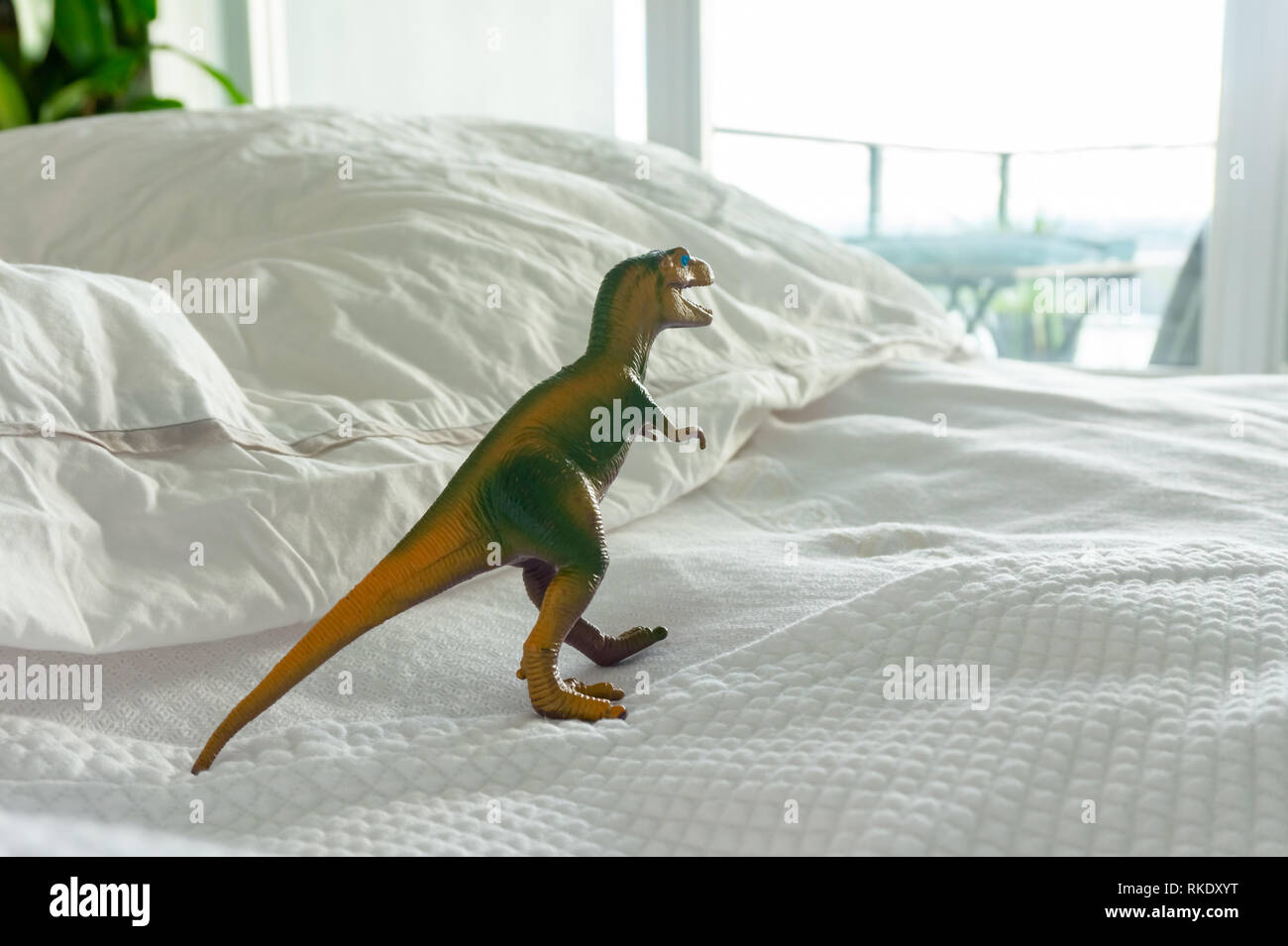 Dinosaure en plastique vert et jaune jouet sur le lit des parents représentant une maison de famille où ils vivent, ou la vie de parent, avoir du plaisir, de l'imagination... Banque D'Images