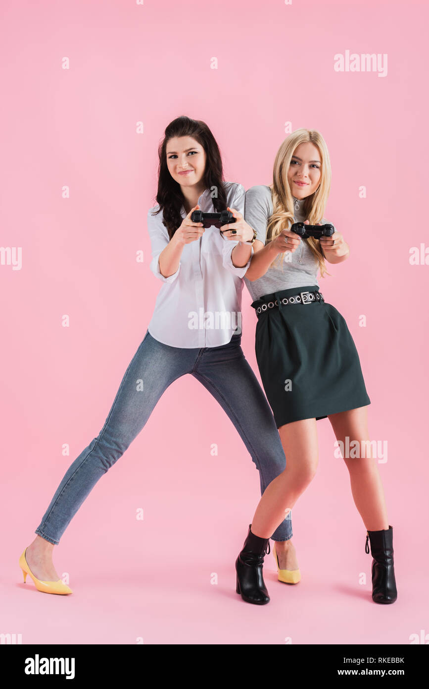 Funny Girls bousculent tout en jouant le jeu vidéo sur fond rose Banque D'Images