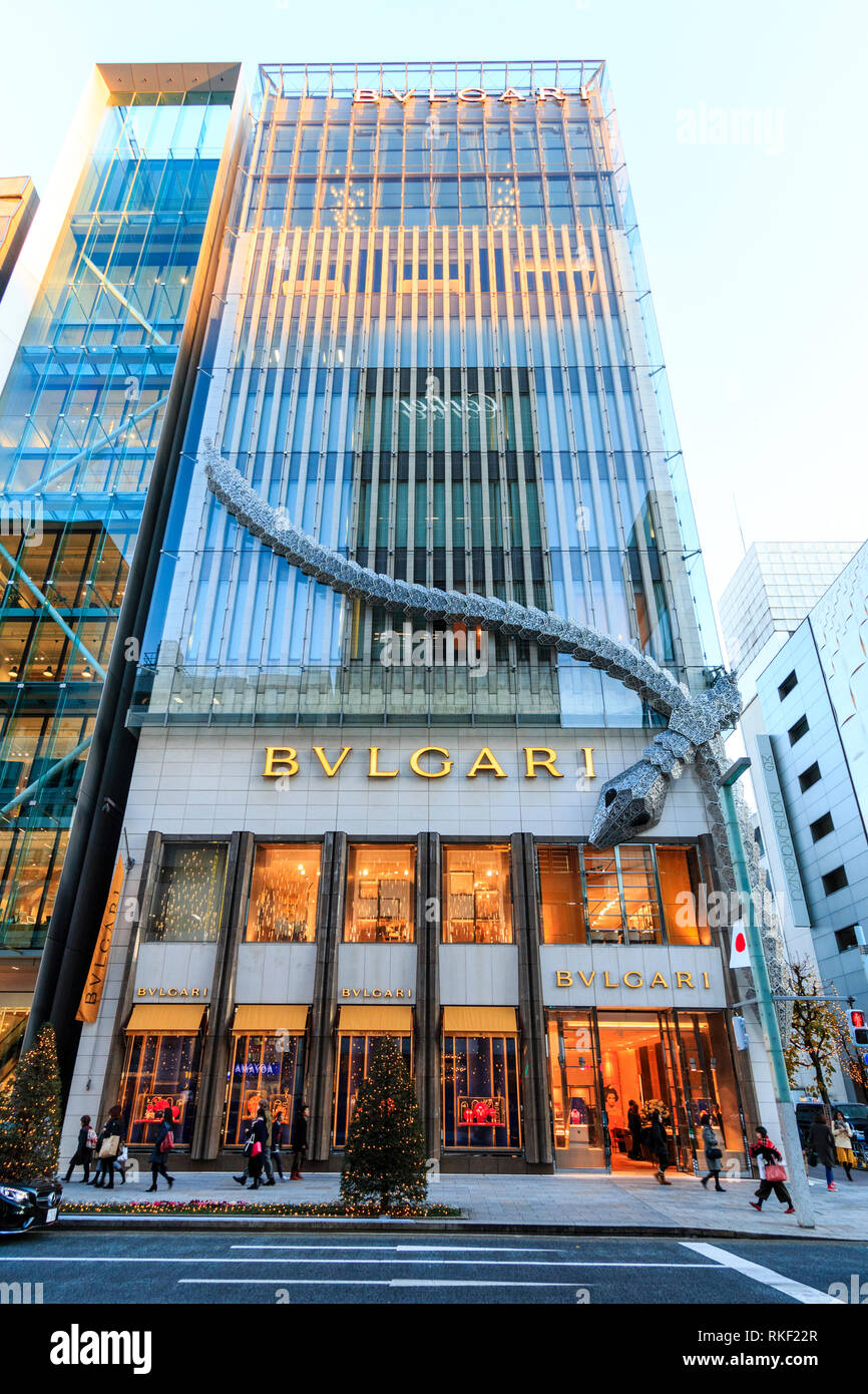 Tokyo, le Ginza. Heure d'or. Le bâtiment Bvlgari avec châssis serpent géant attaché à coin. Les arbres de Noël lumineux sur la chaussée. Banque D'Images