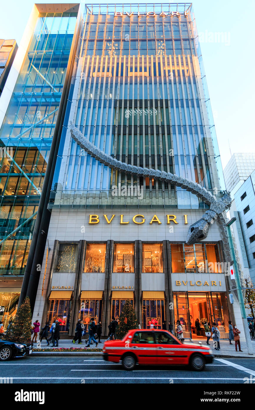 Tokyo, le Ginza. Heure d'or. Le bâtiment illuminé Bvlgari avec châssis serpent géant attaché à coin. Conduite de taxi rouge passé, de flou. Banque D'Images
