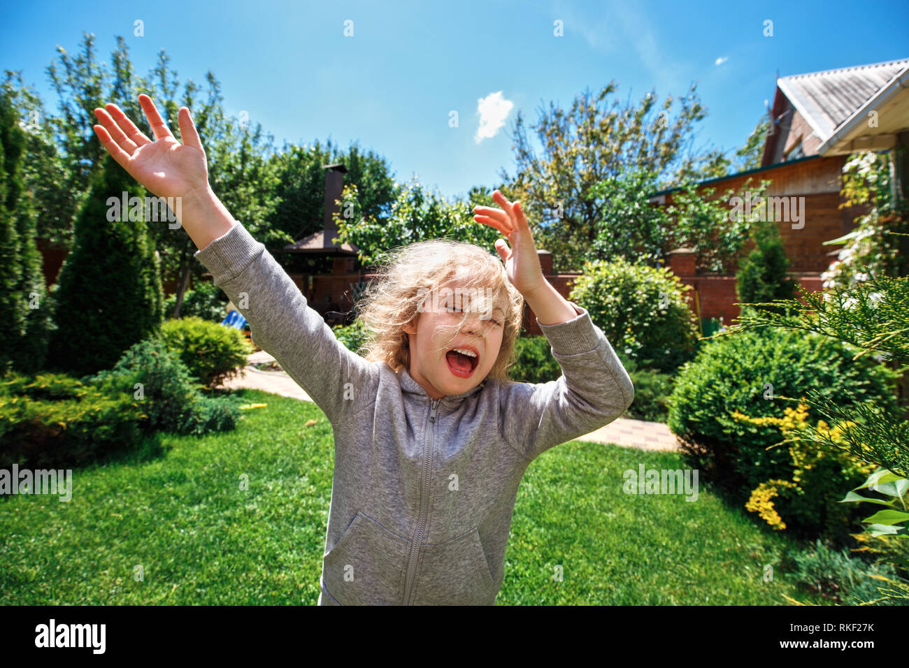 Petite fille blonde gaie s'amuse sur la pelouse près de sa maison Banque D'Images