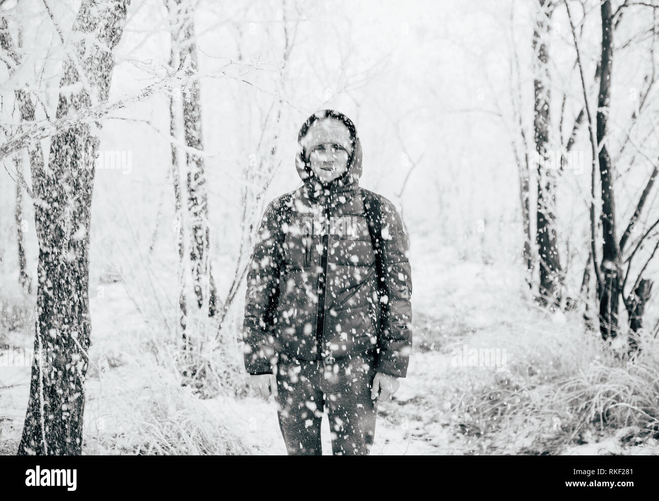 Un gars portant une chemise avec un capot est debout dans une forêt enneigée, la neige tombe sur lui à partir de ci-dessus. Photo en noir et blanc Banque D'Images Un gars portant une chemise avec un capot est debout dans une forêt enneigée, la neige tombe sur lui à partir de ci-dessus. Photo en noir et blanc Banque D'Images