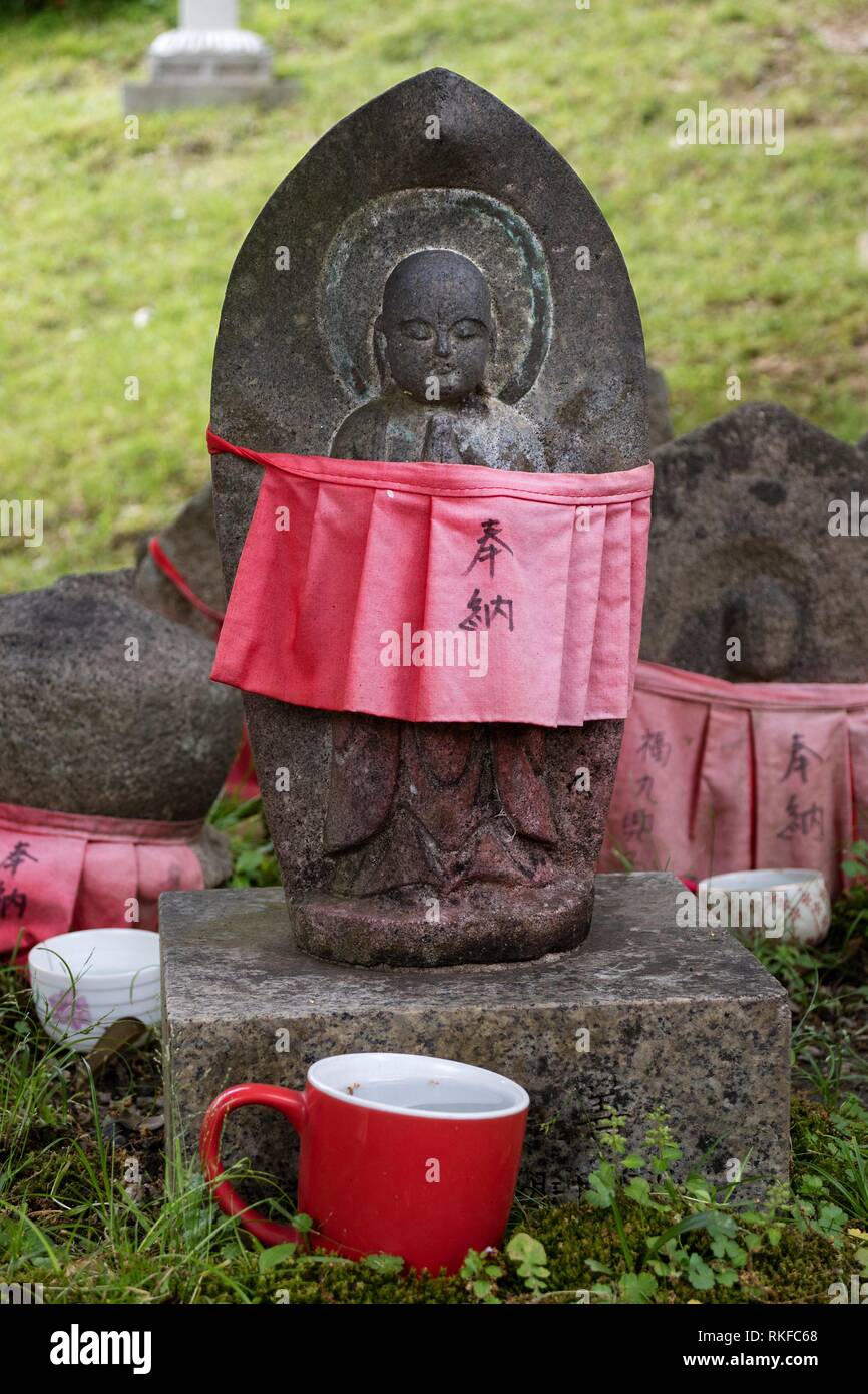 Sculpté en pierre traditionnelle avec Jizo jupe rouge honoré et respecté avec une tasse d'eau. Banque D'Images