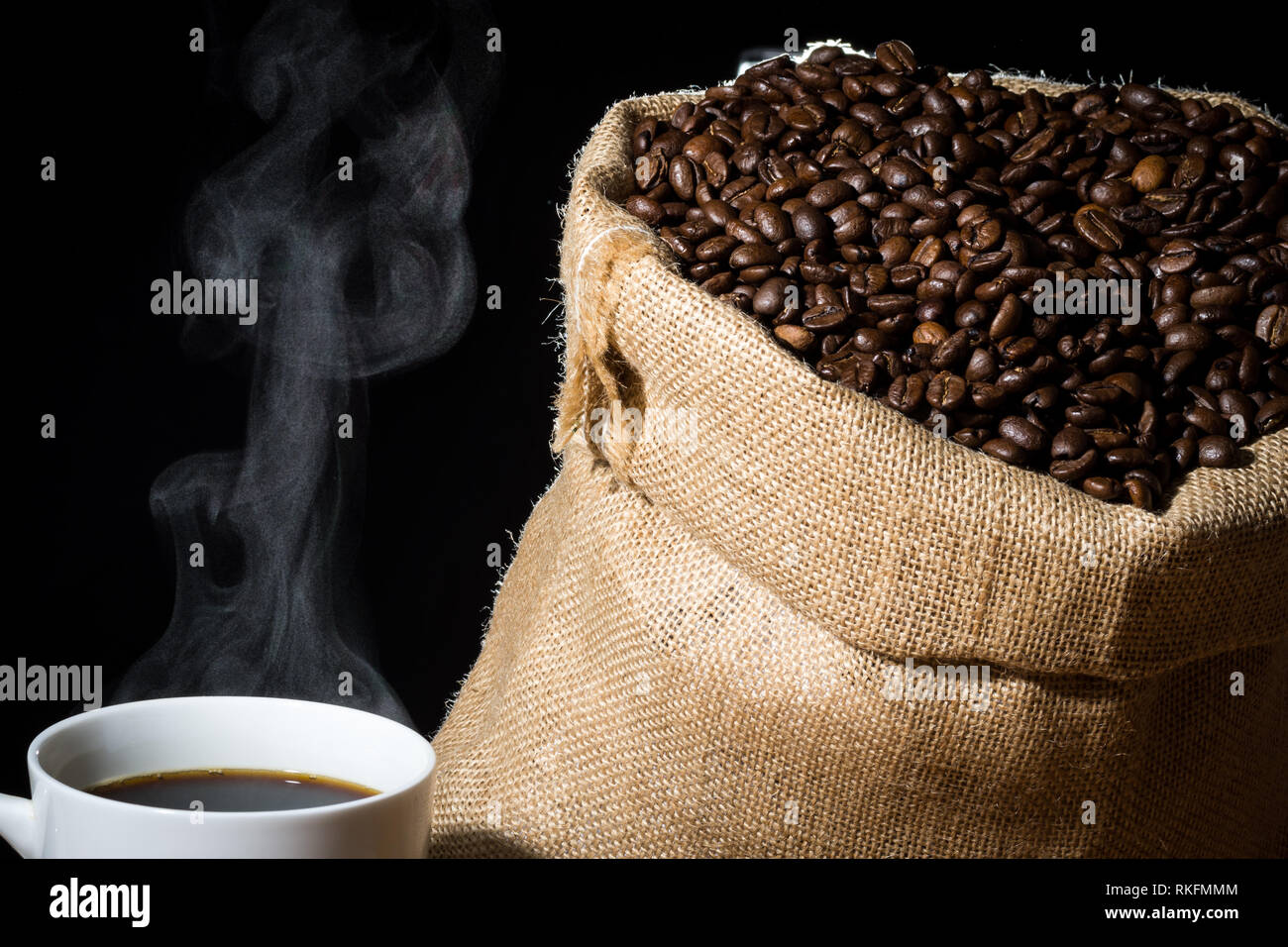 Café infusé dans une tasse blanche avec de la vapeur ou de la vapeur et les grains de café dans un sac en toile de jute jute dans l'arrière-plan. Banque D'Images