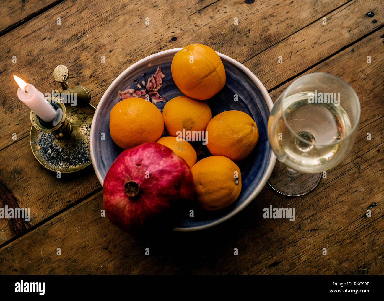 Table en bois avec porte-bougie en laiton verre de vin et un bol avec des oranges et de grenadier Banque D'Images