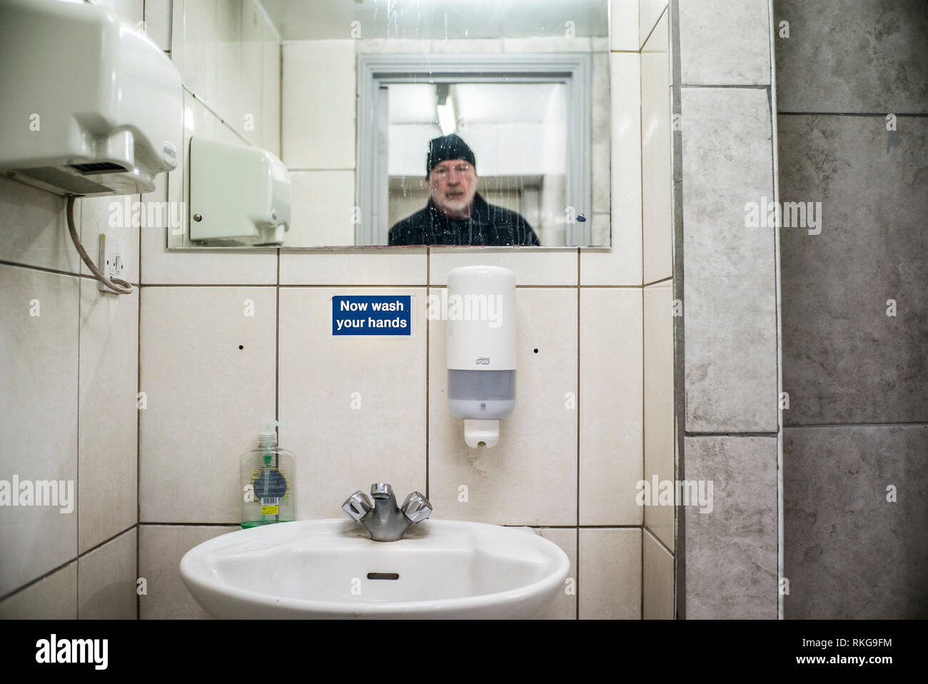 Homme barbu en miroir, se laver les mains maintenant signer, toilettes publiques, sèche-mains, distributeur de savon liquide, Banque D'Images