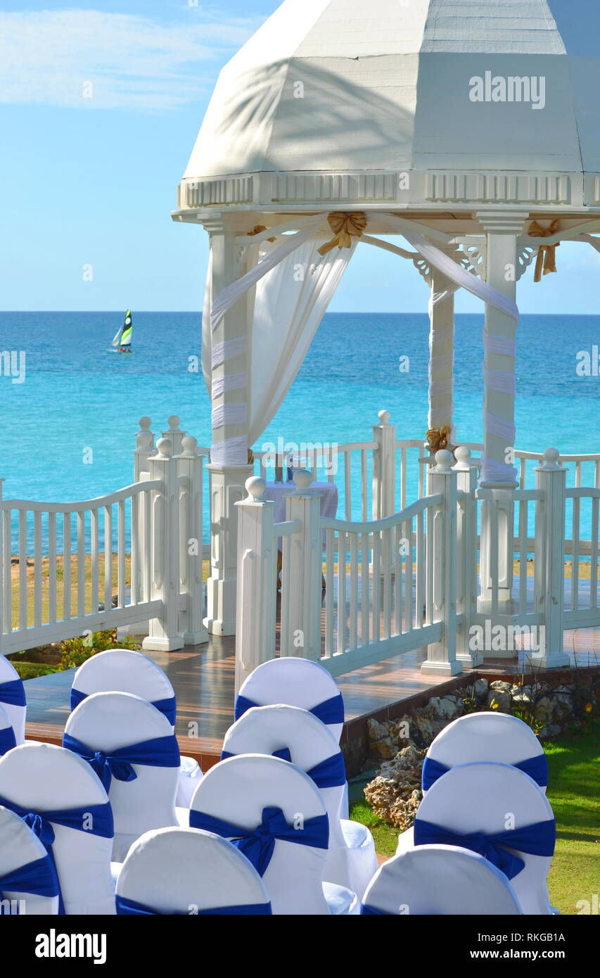 Gazebo de mariage blanc dans un jardin tropical balnéaire lors d'une réception de mariage de destination avec des chaises décorées alignés pour une cérémonie civique. Banque D'Images