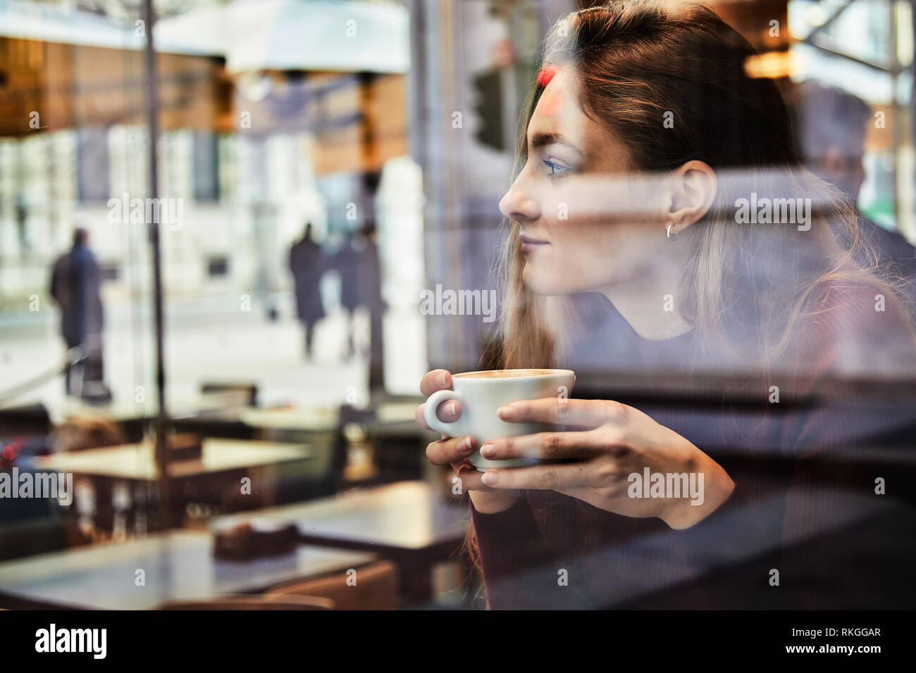 Girl daydreaming tandis que détient une tasse de café au café du coin, concept photo au travers de la fenêtre de l'effet de la ville avec la réflexion Banque D'Images