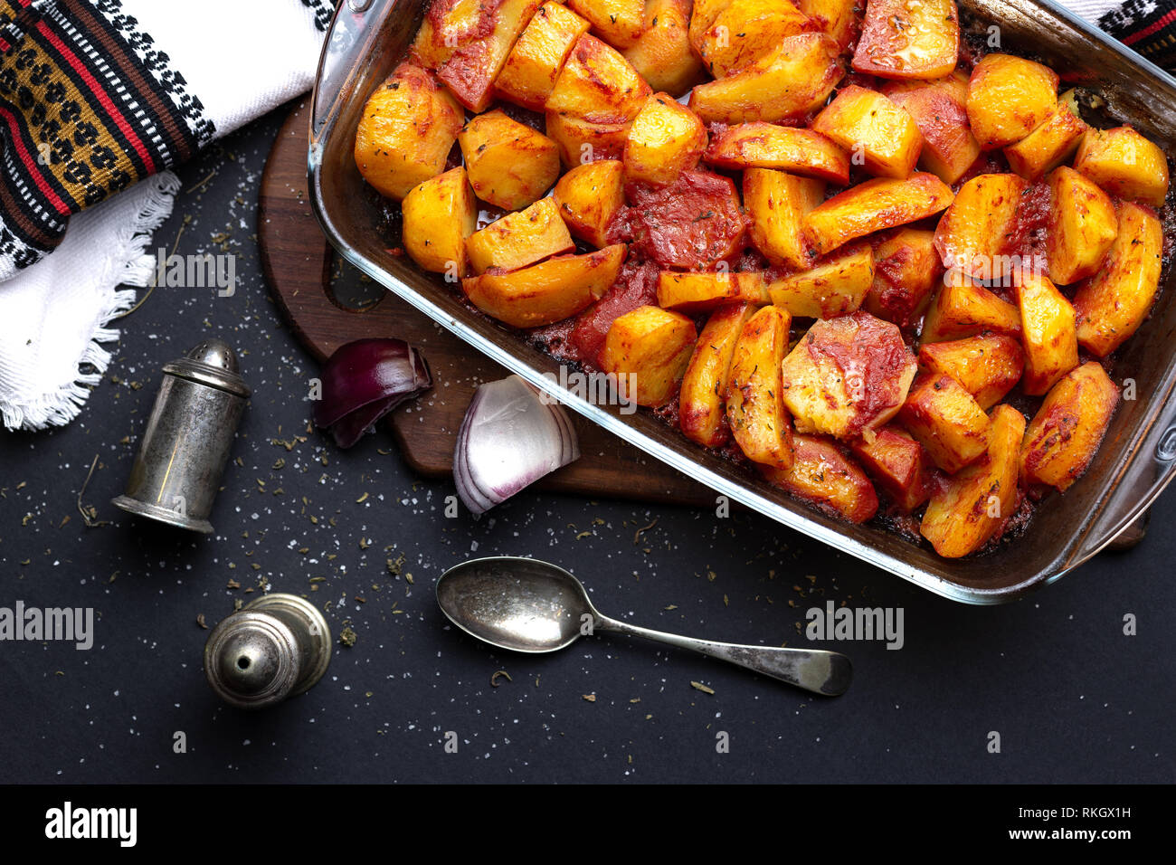 Les pommes de terre cuites au four avec des épices et du jus de tomates sur la plaque de cuisson en verre sur table noire Banque D'Images