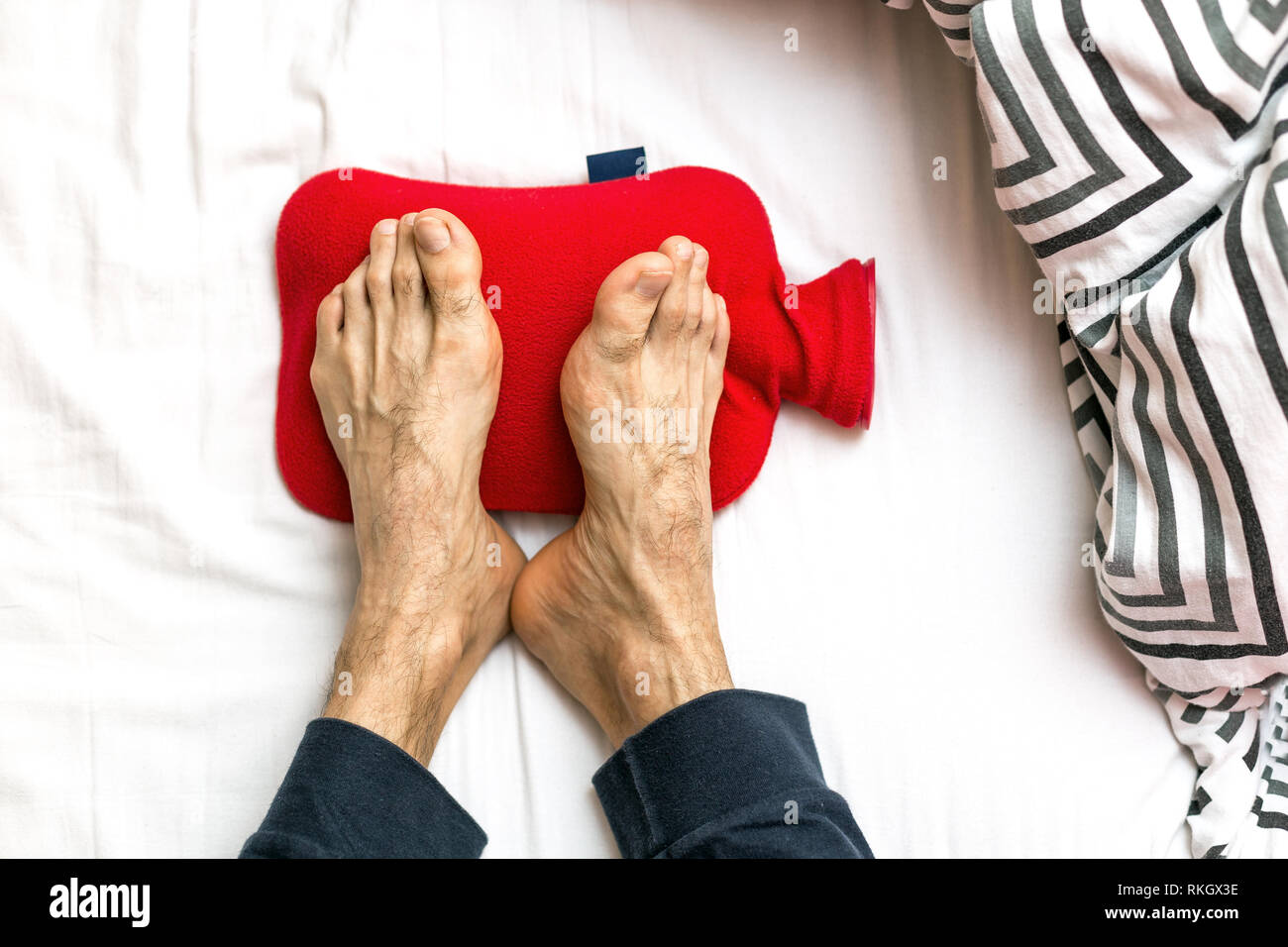 Homme avec des pieds froids dans le lit sur une bouteille d'eau chaude  rouge. Le réchauffement des pieds froids Photo Stock - Alamy