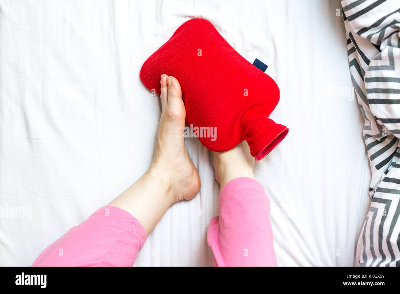 Femme avec des pieds froids dans le lit sur une bouteille d'eau chaude rouge. Le réchauffement des pieds froids concept avec place pour le texte Banque D'Images