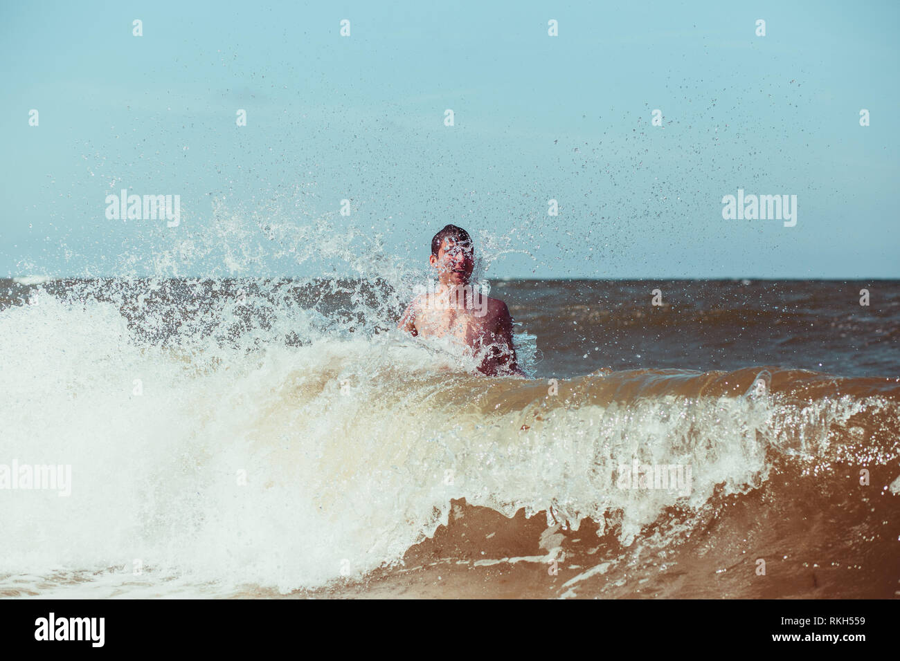 Jeune homme appréciant les vagues dans la mer lors d'une vacances d'été. Passer un des vacances à la mer Banque D'Images