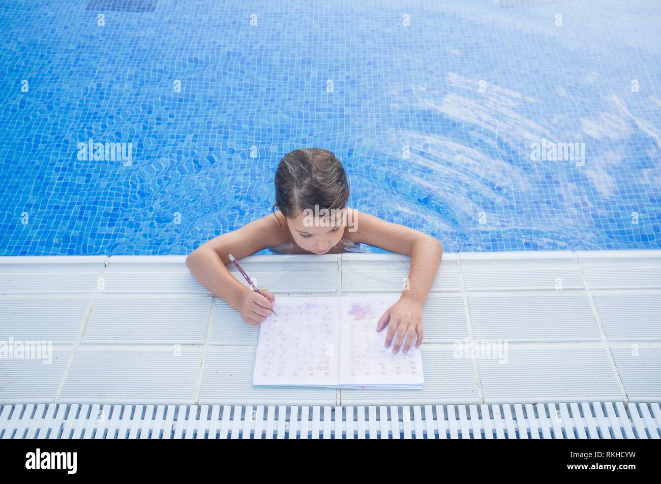 Fille enfant faisant plus de devoirs de vacances au bord de la piscine. Devoirs d'été pour les enfants. concept Banque D'Images