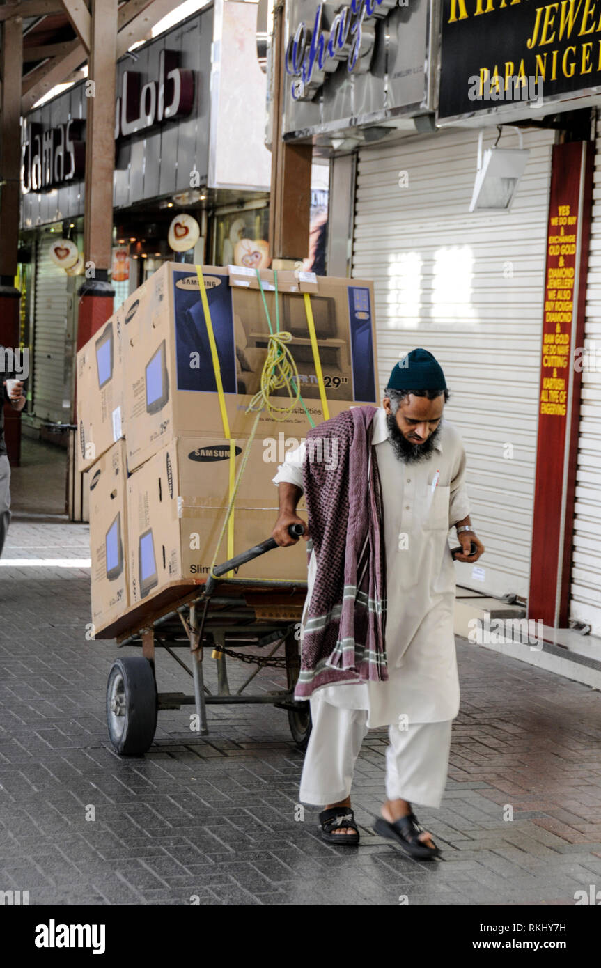 Un ouvrier asiatique tirant son panier faire une livraison de télévision pour l'un des petits détaillants dans le Gold Souk de Dubaï situé dans le quartier o Banque D'Images