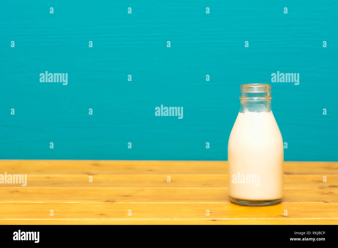 Lait Crème fraîche dans un tiers de pinte de lait, bouteille en verre sur une table en bois contre un arrière-plan peint sarcelles lumineux Banque D'Images
