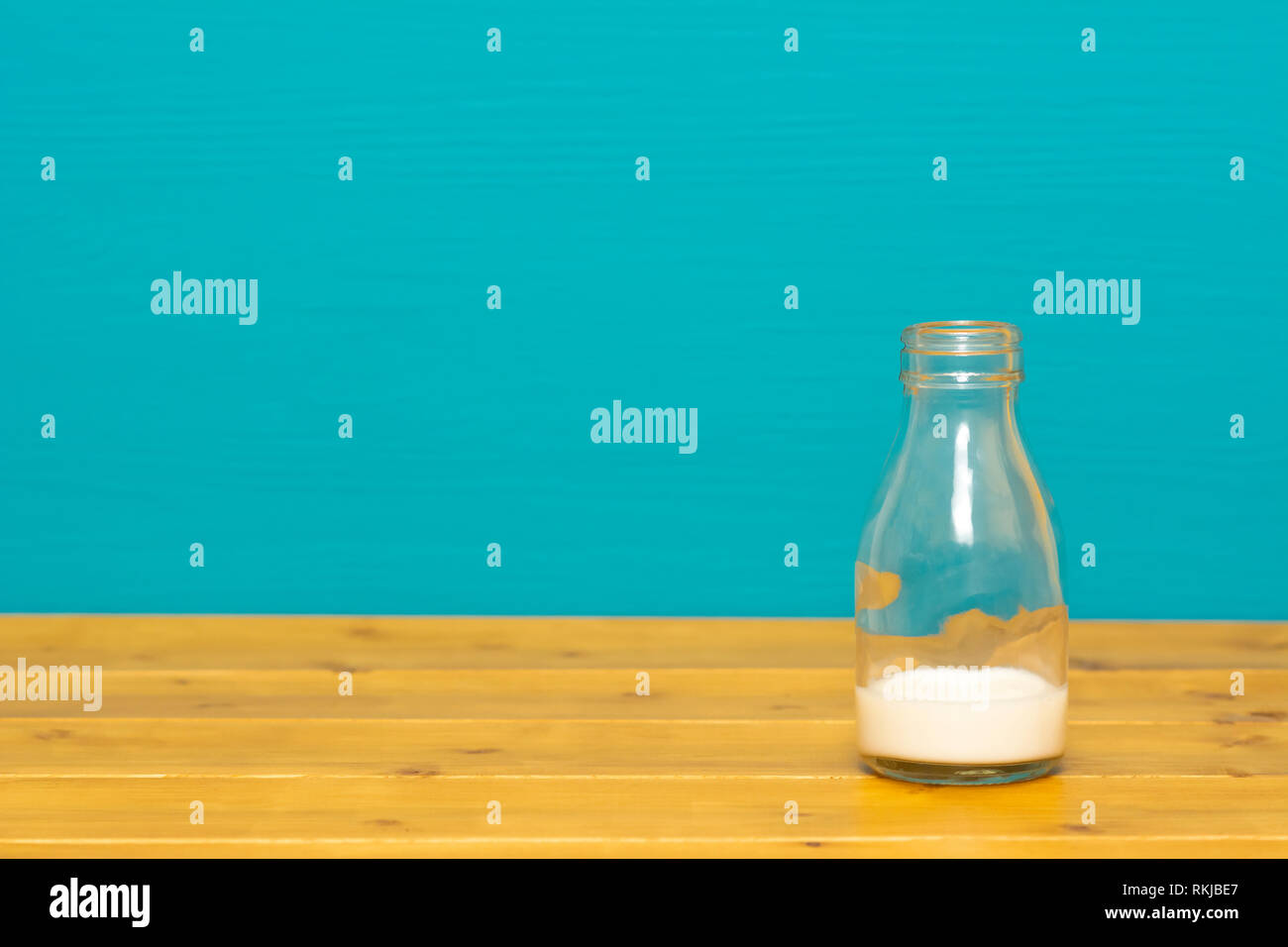 Un tiers de pinte de lait en verre bouteille avec racaille du lait crémeux frais, sur une table de bois contre un arrière-plan peint sarcelles lumineux Banque D'Images