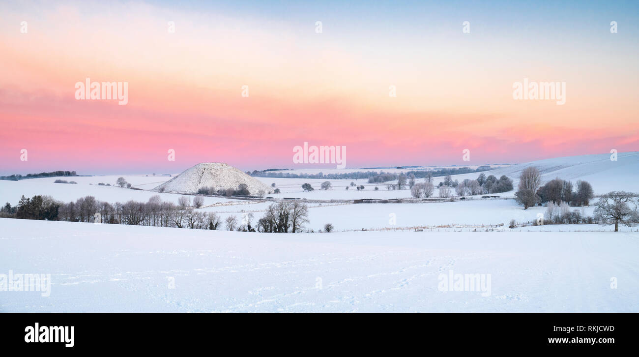 Silbury Hill dans la neige de l'hiver au crépuscule avant le lever du soleil. Avebury, Wiltshire, Angleterre. Vue panoramique Banque D'Images