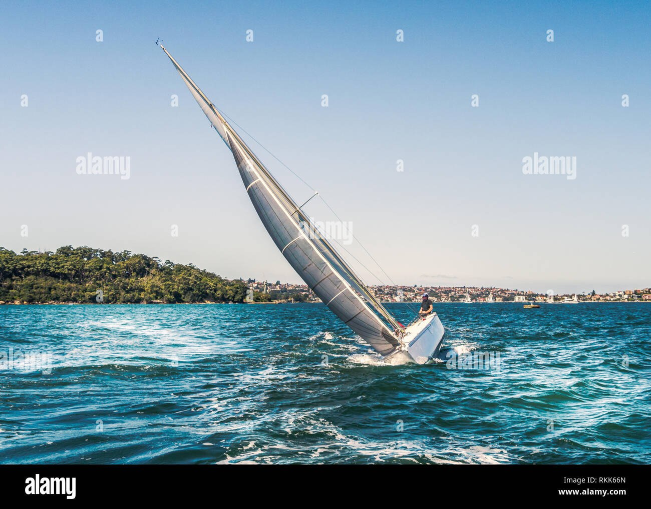 Une location de gîte, basculant dans l'eau qu'il dispose d'un grand voile gris argent et est coupant à travers les eaux bleues de la baie de Sydney, Australie sur une d'été Banque D'Images