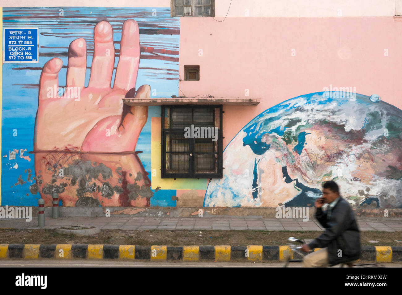 Man rides passé une murale intitulée sous les mains de l'artiste Gaia, dans Lodhi Colony, New Delhi, Inde Banque D'Images