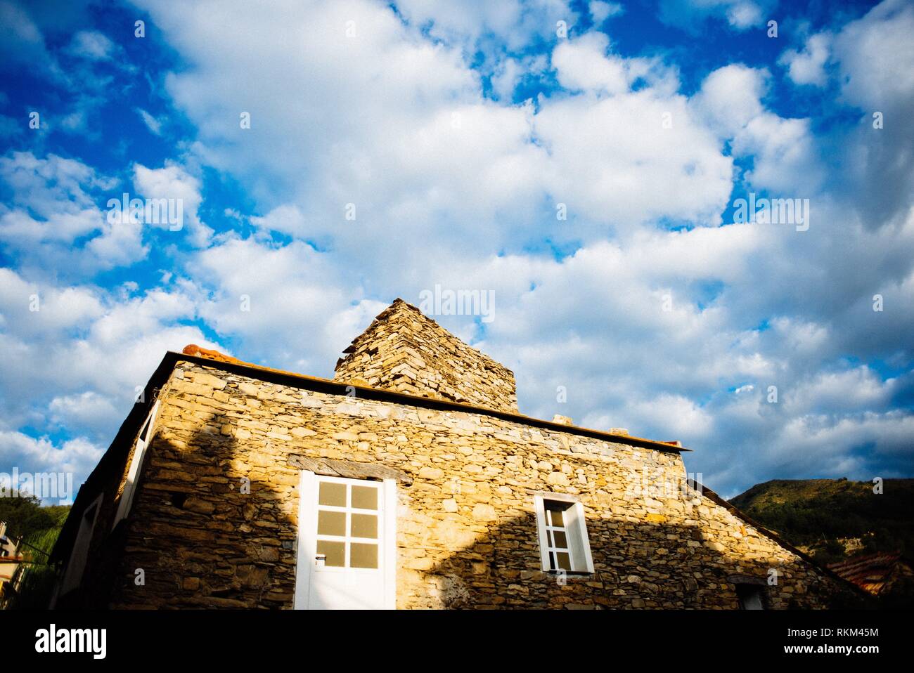 Maison ancienne en pierre illuminé par le soleil levant dans un ancien village de Ligurie prises à partir de la faible ciel bleu et nuages blancs. Banque D'Images